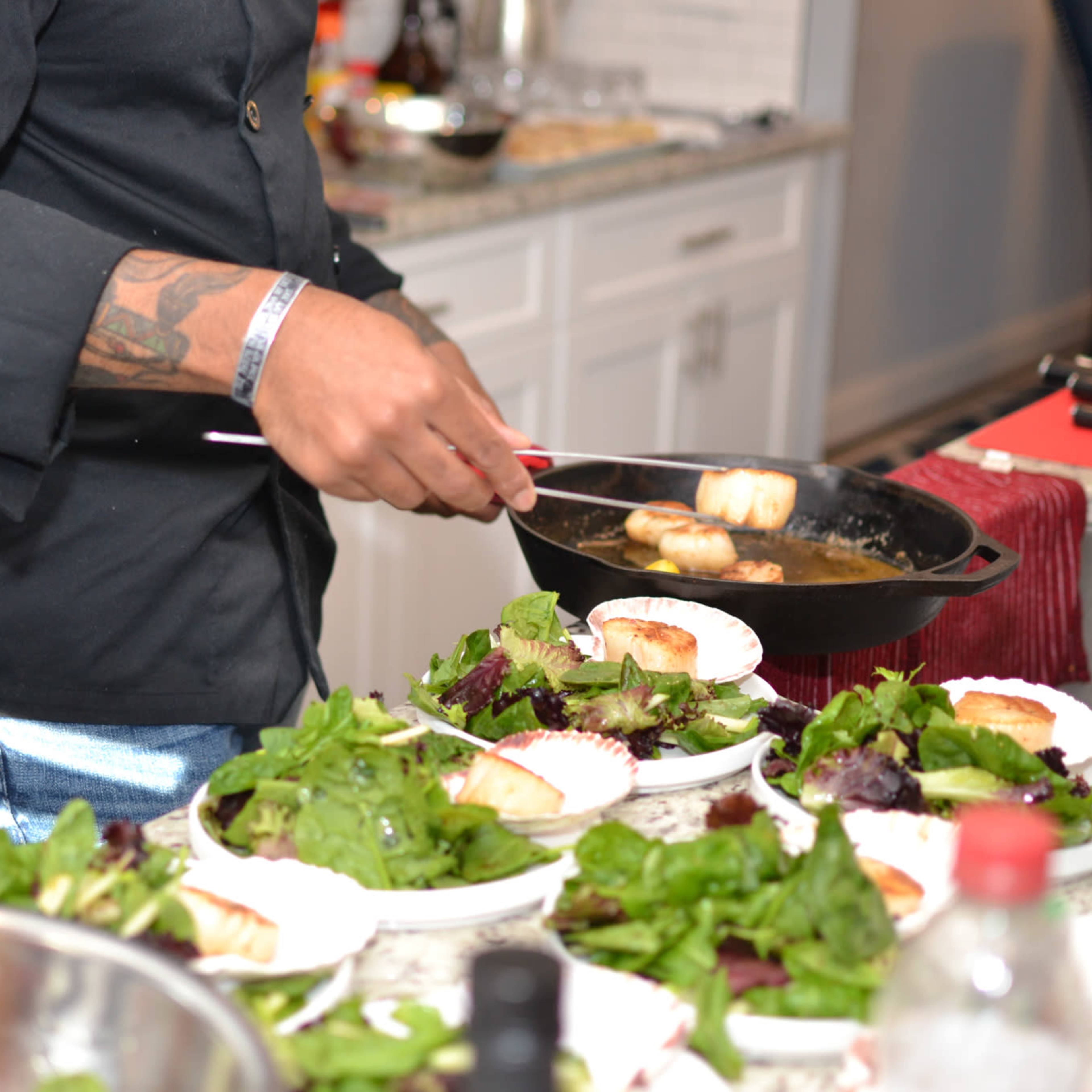A chef serves sautéed fish onto plates of mixed salad in a kitchen.