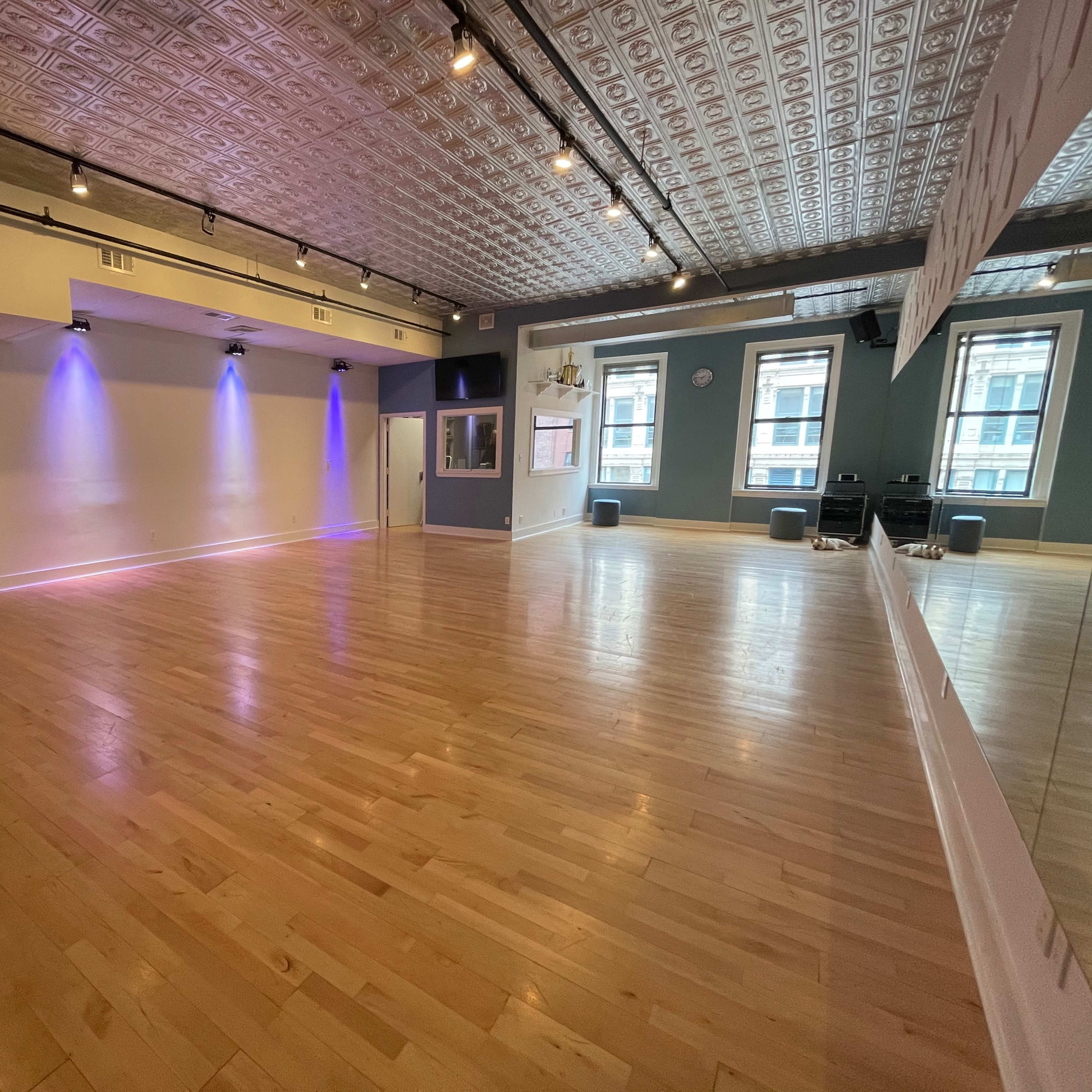 A spacious studio with wooden flooring, wall-mounted mirrors, and soft lighting.