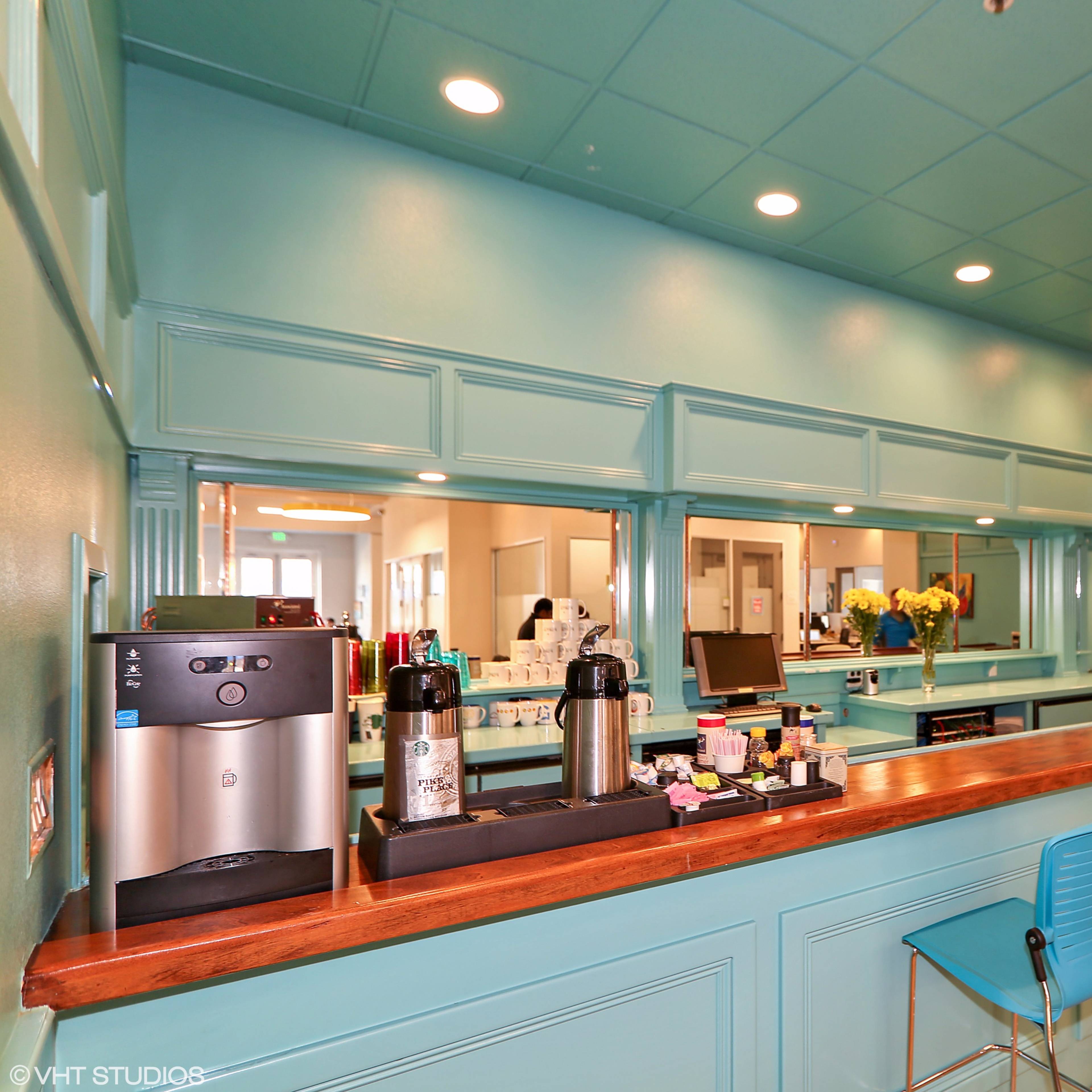 A brightly colored room with a turquoise wall, a wooden counter, and several coffee machines and seating.