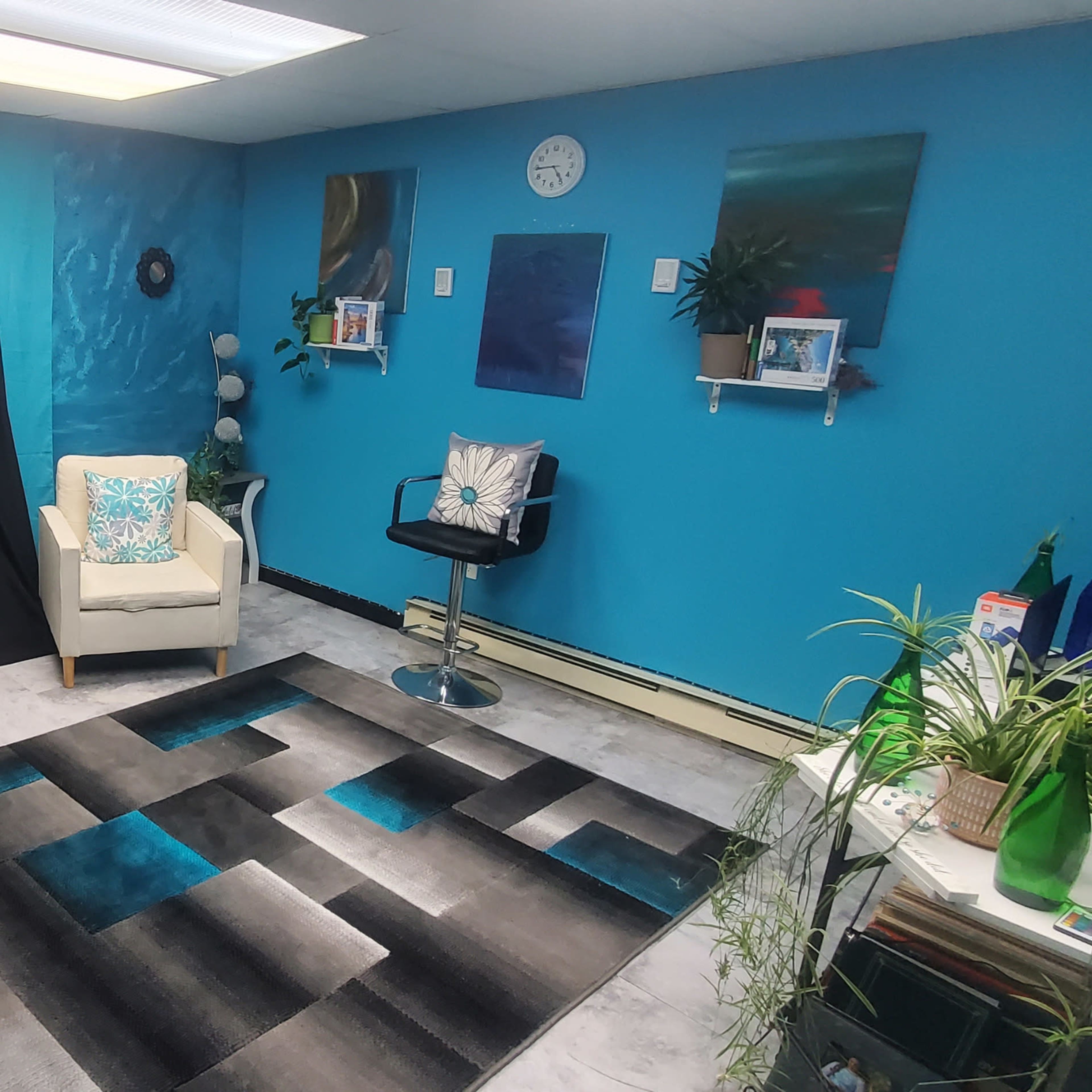 A bright blue room with two white chairs and a bar stool, a patterned rug, and various wall decorations, including plants and shelves.