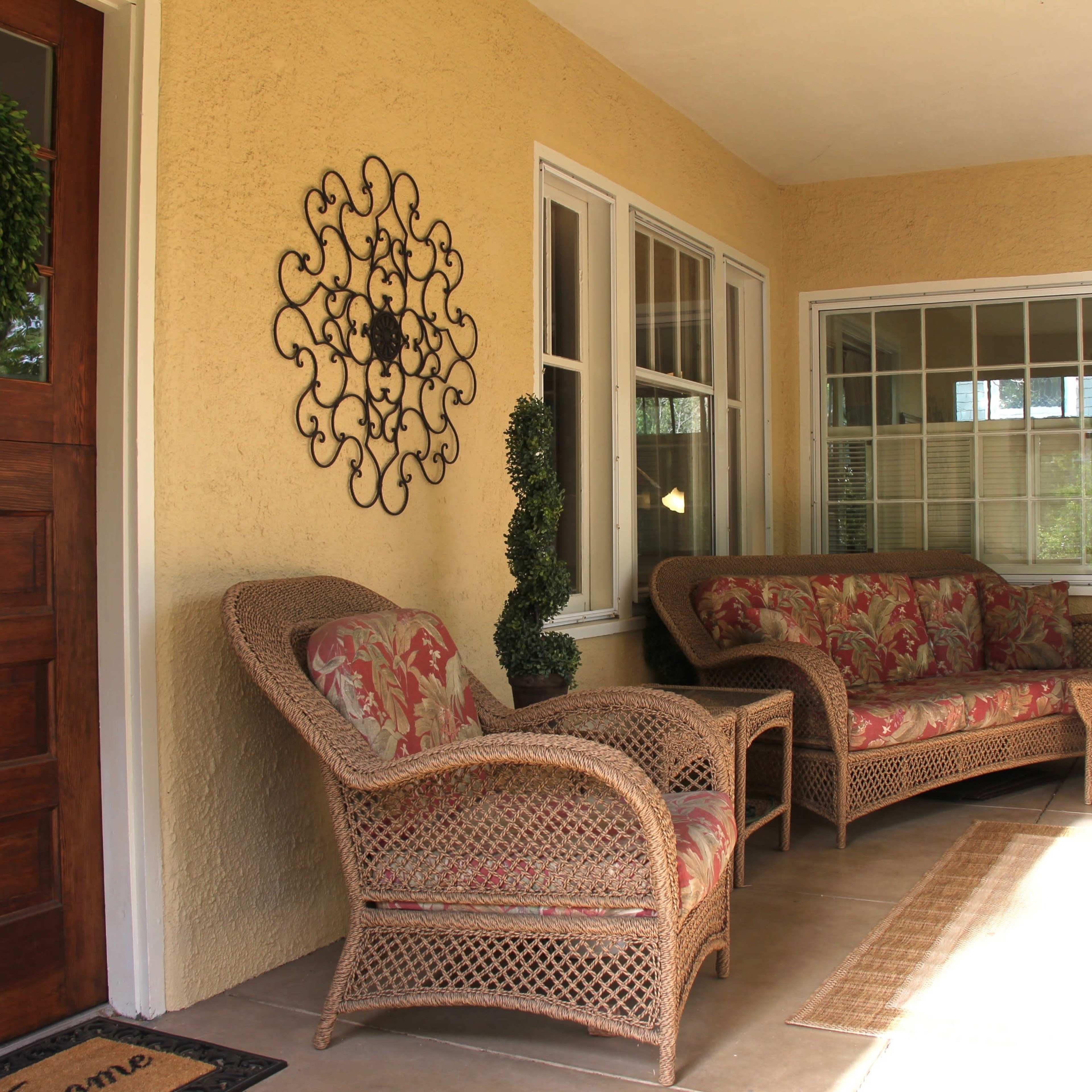 A porch area with a wicker seating arrangement, a decorative wall piece, and a wooden front door.