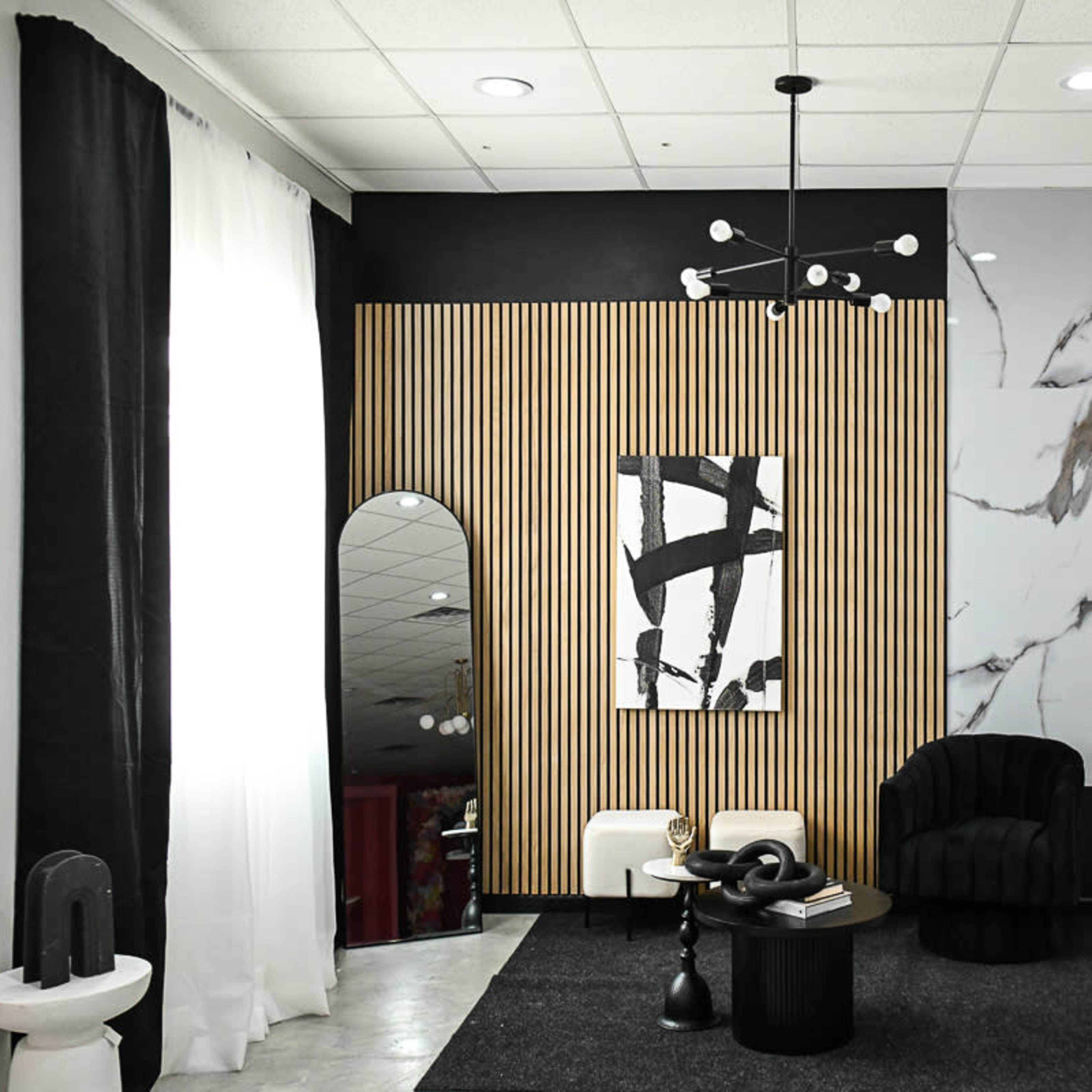 A modern interior space with a black wall, a marbled feature wall, wooden paneling, a round mirror, a black accent chair, and decorative plants.