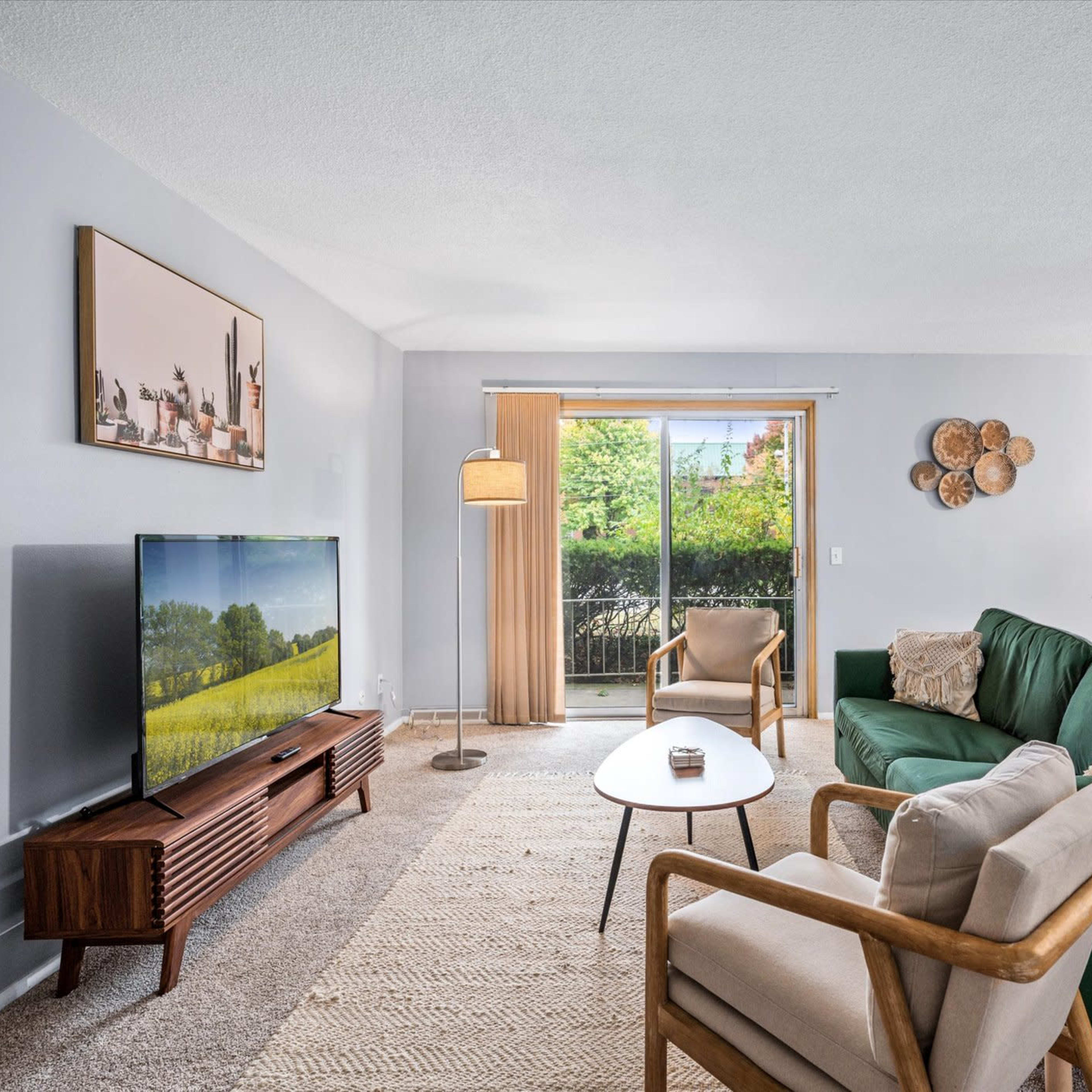 A living room with a television, green sofas, a wooden table, and a sliding door leading to a patio.