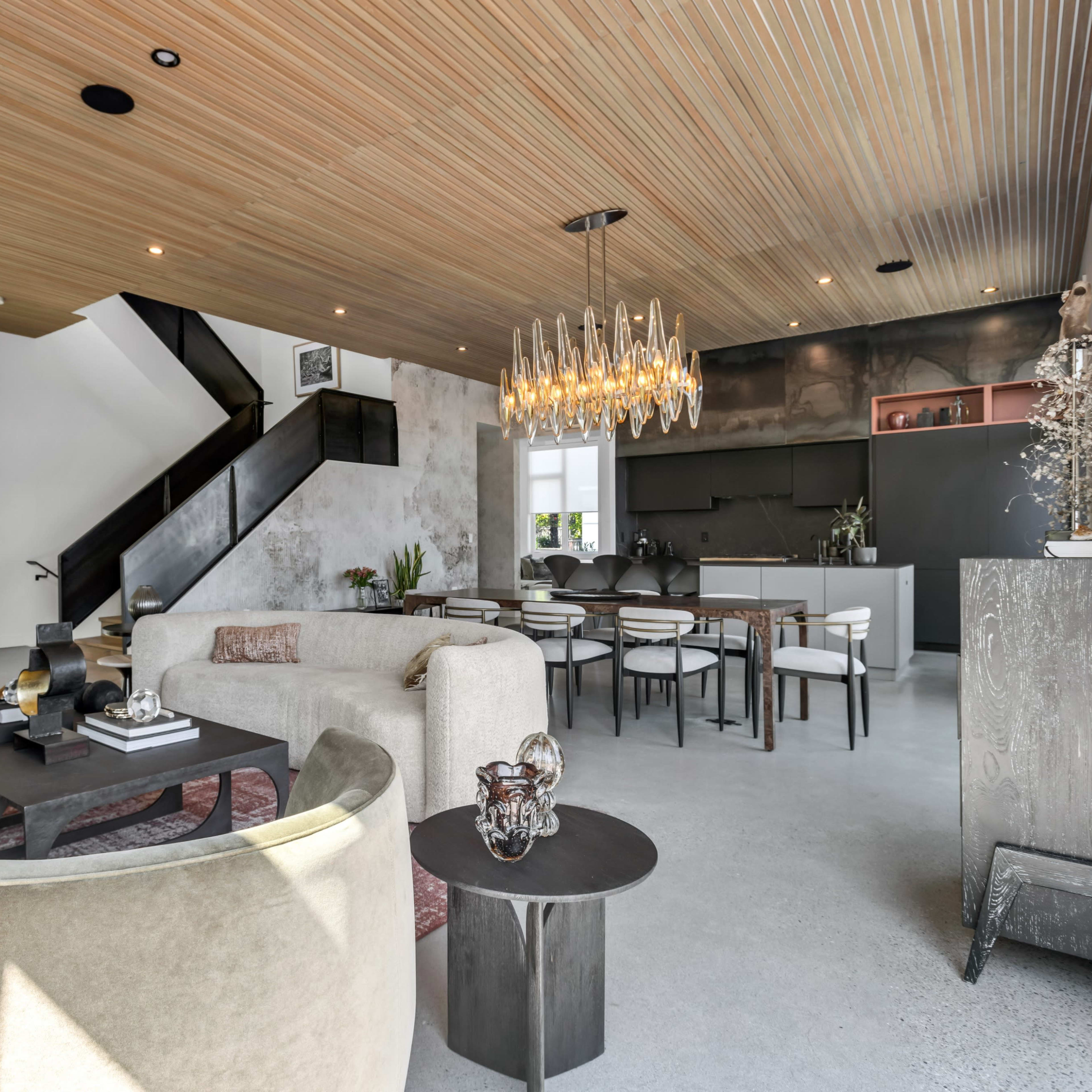 A modern open-concept living area featuring a light-colored sofa, a dining table with chairs, and a sleek kitchen in the background.