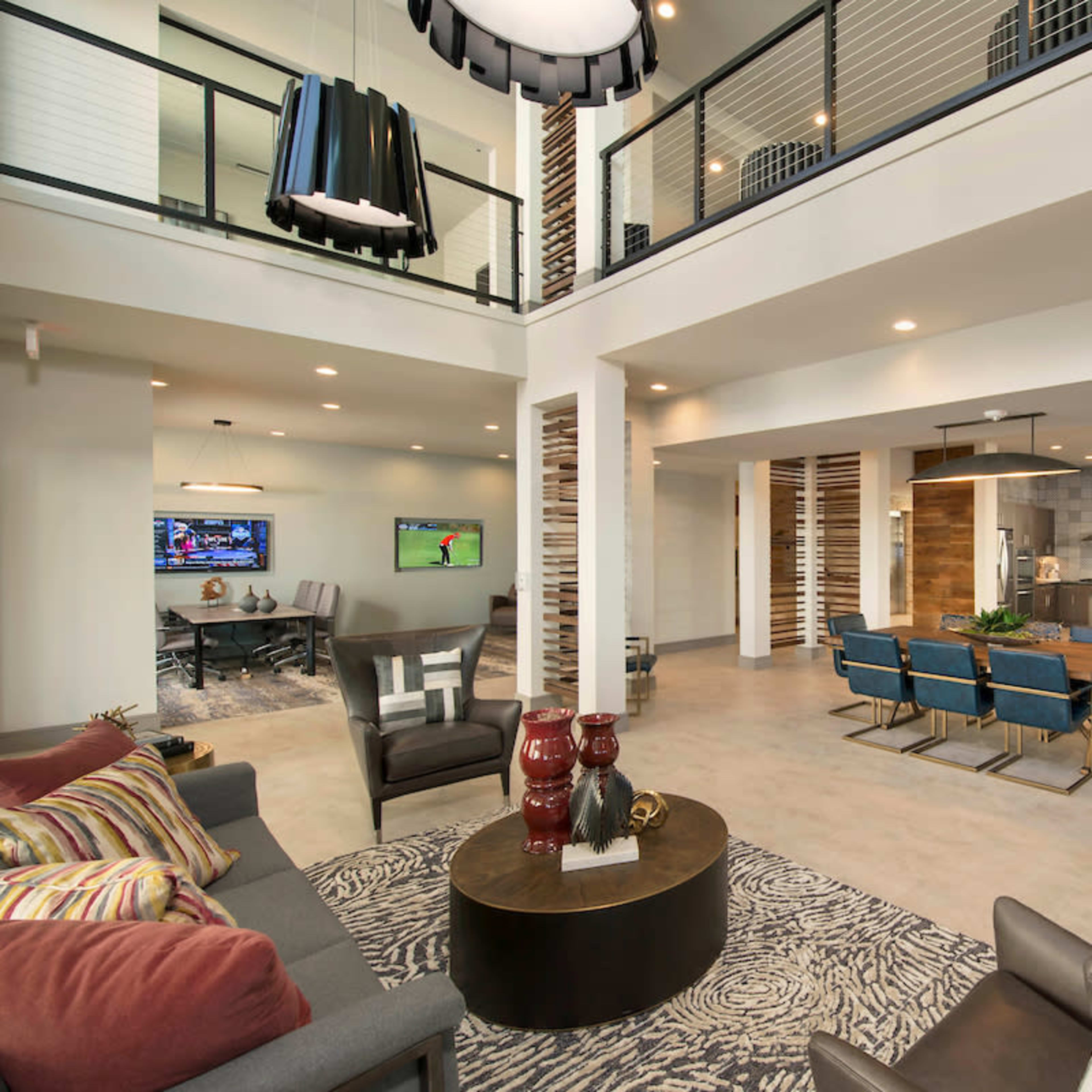 A modern open-plan living area featuring a seating space with a gray sofa, a round coffee table, and a dining area with blue chairs and a large table.