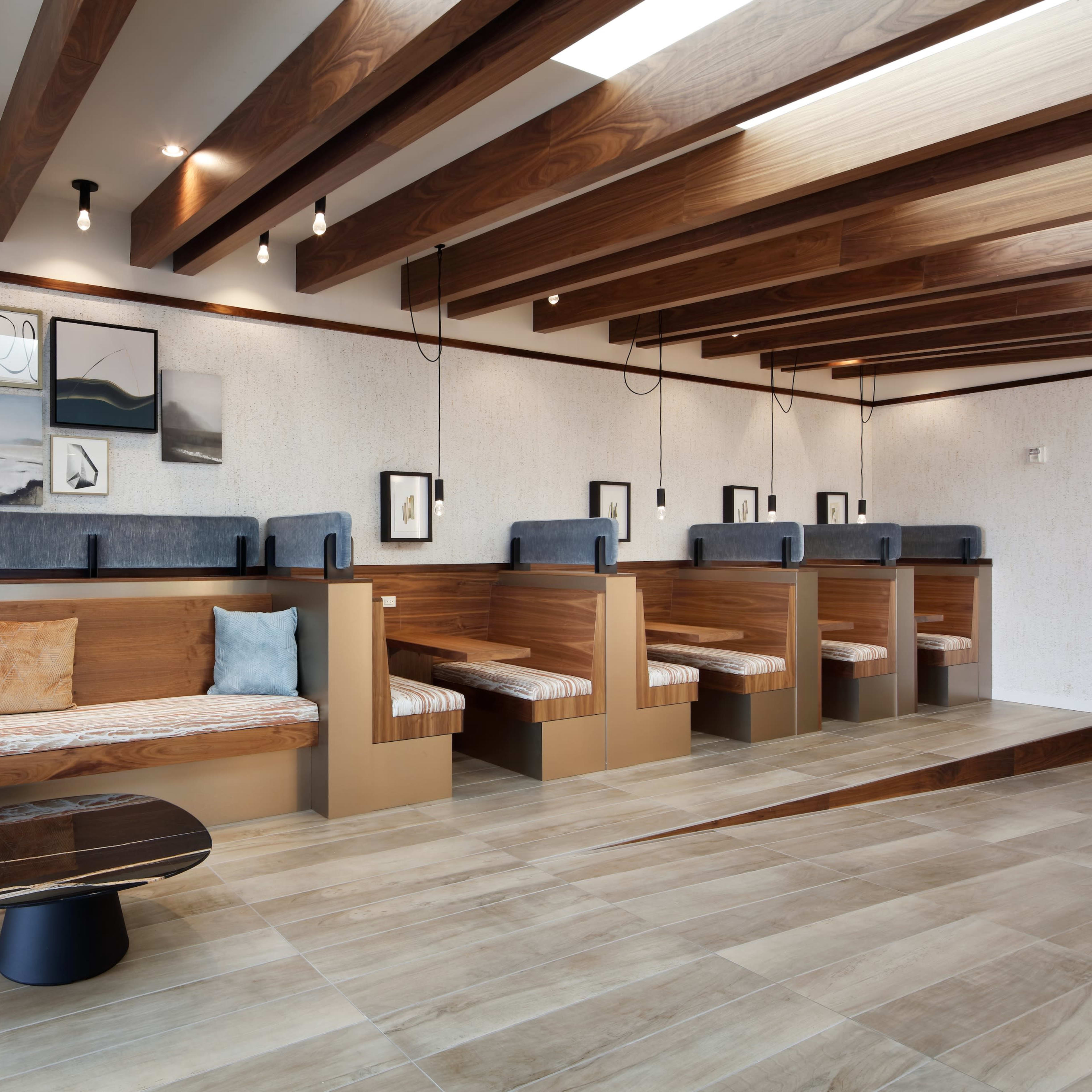 A modern interior space featuring wooden beams, seating areas with cushions, and framed artwork on the walls.