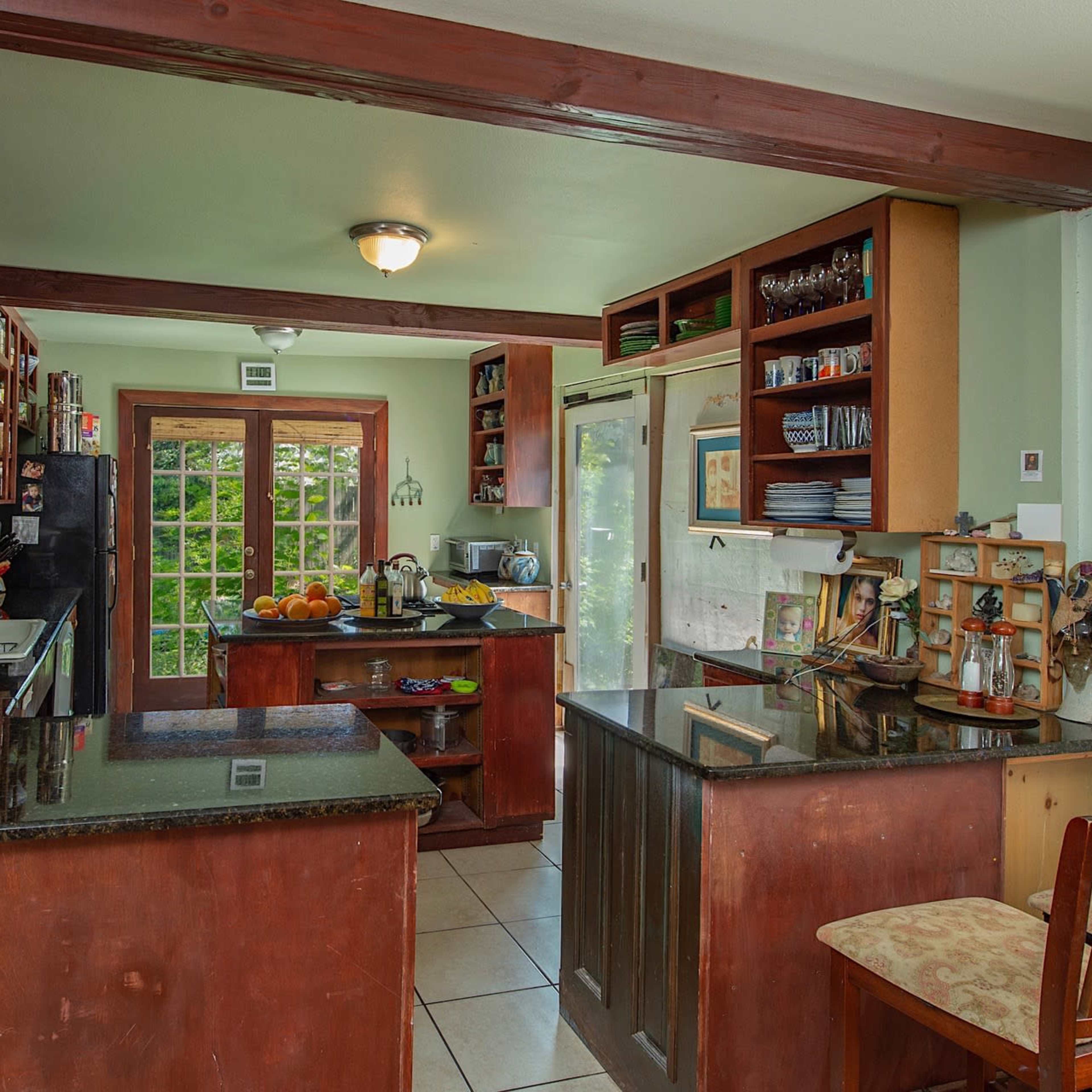 A modern kitchen with wooden cabinetry, a black countertop, and a dining area featuring a stool.