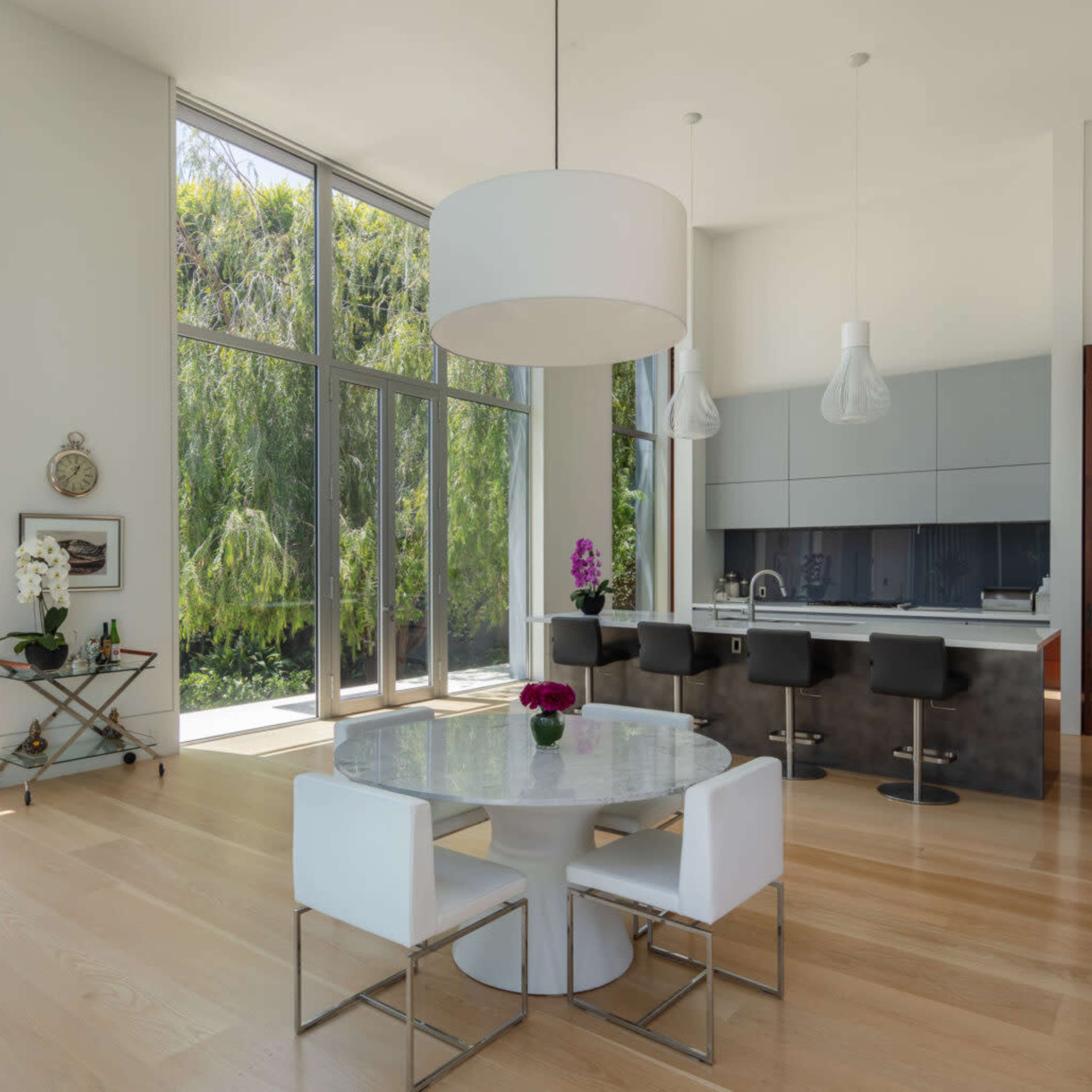 A modern kitchen and dining area with large windows, a round table, and sleek bar stools.