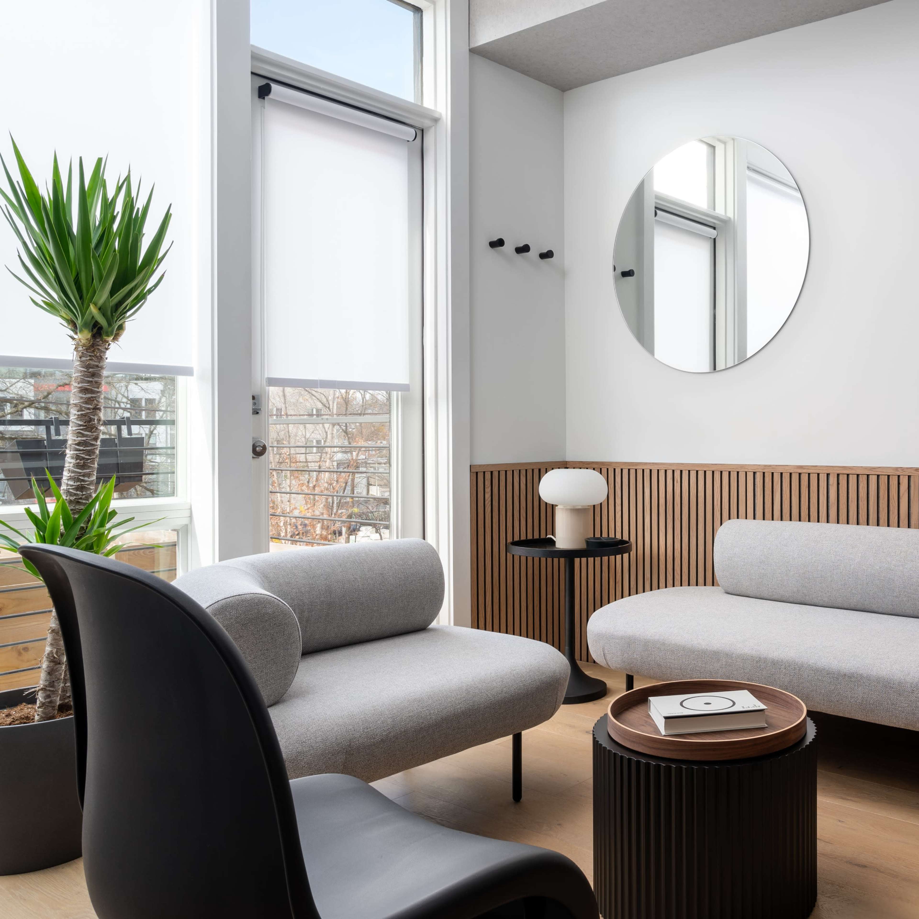 A modern lounge area with a light gray sofa, two circular mirrors on the wall, a black chair, and a round coffee table.