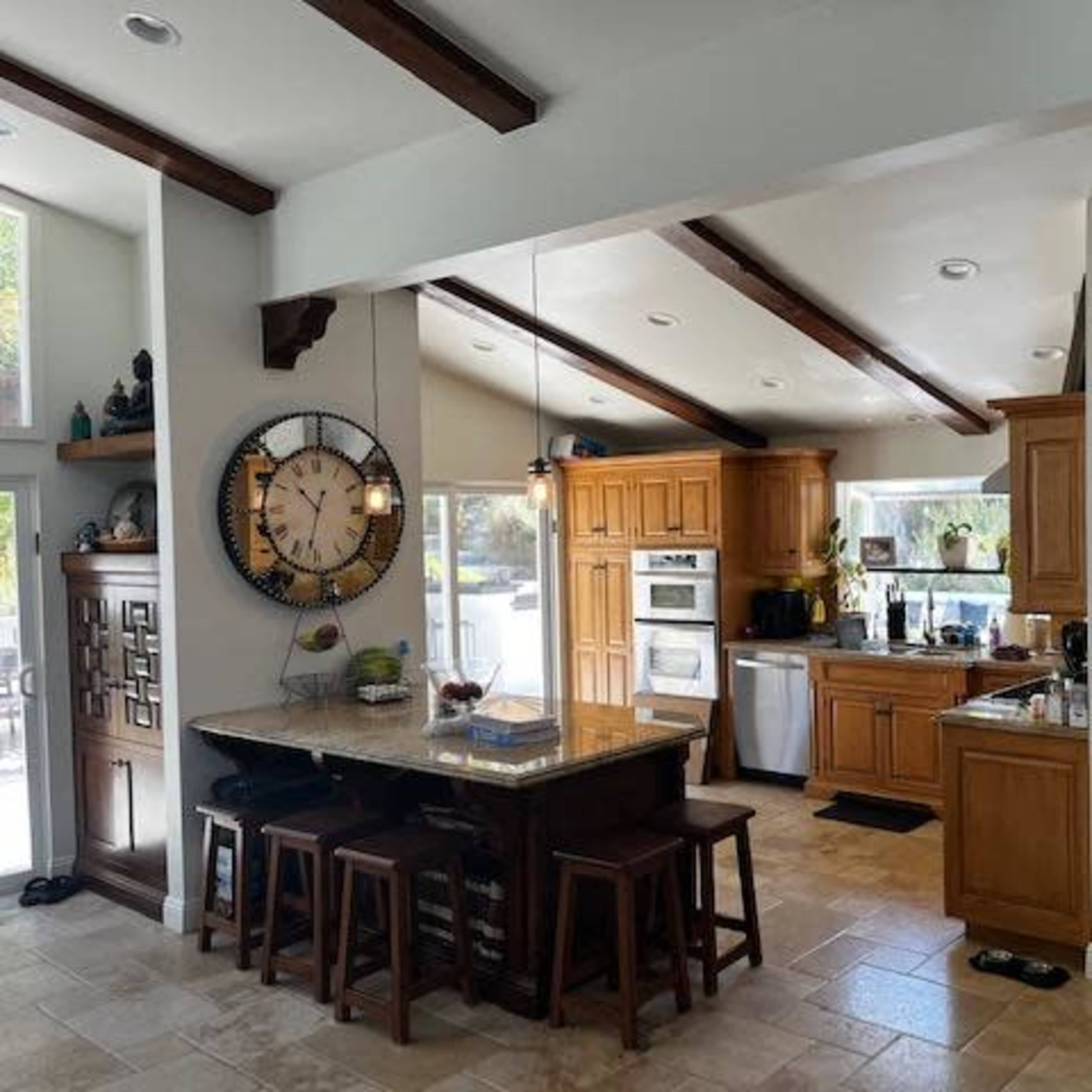 A spacious kitchen with wooden cabinets, a central island with seating, and large windows allowing natural light to enter.