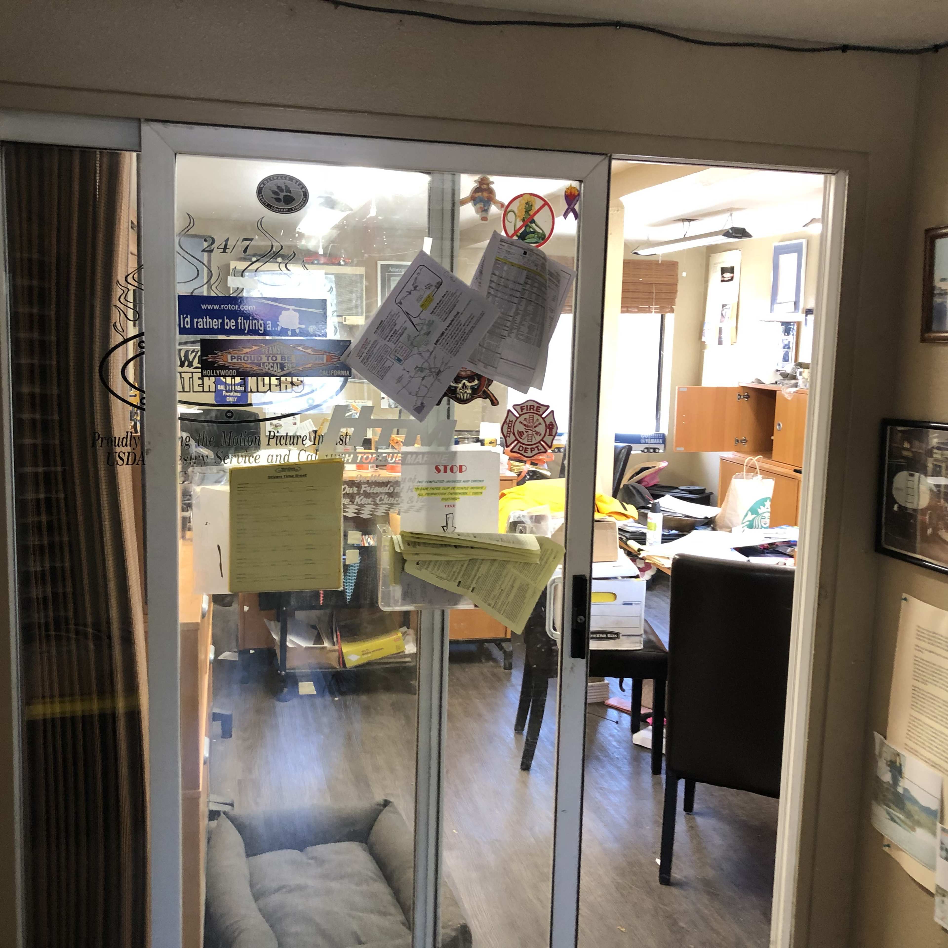A glass door leading into an office space cluttered with papers, boxes, and furniture.