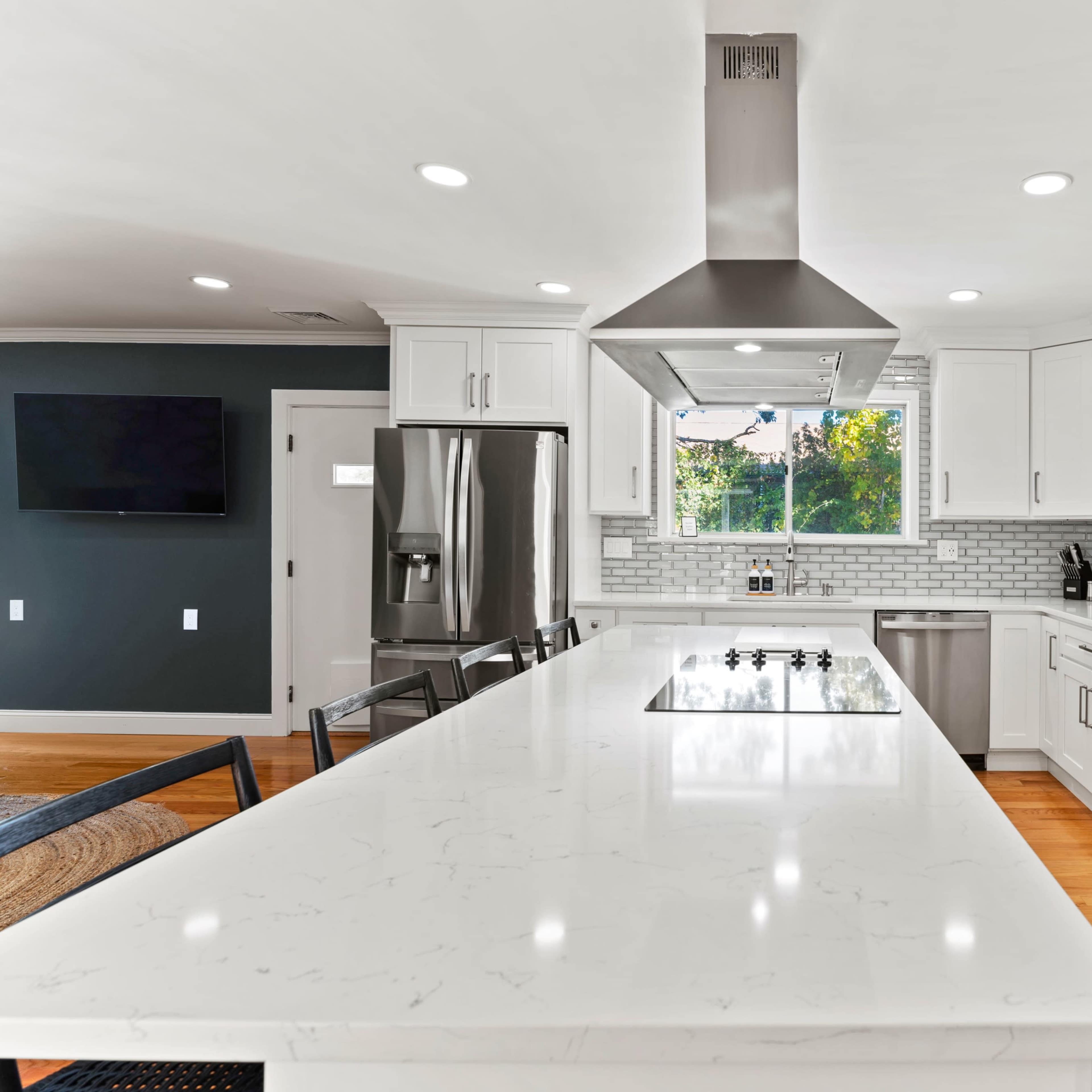 A modern kitchen featuring white cabinetry, stainless steel appliances, and a large island with a cooktop and seating.