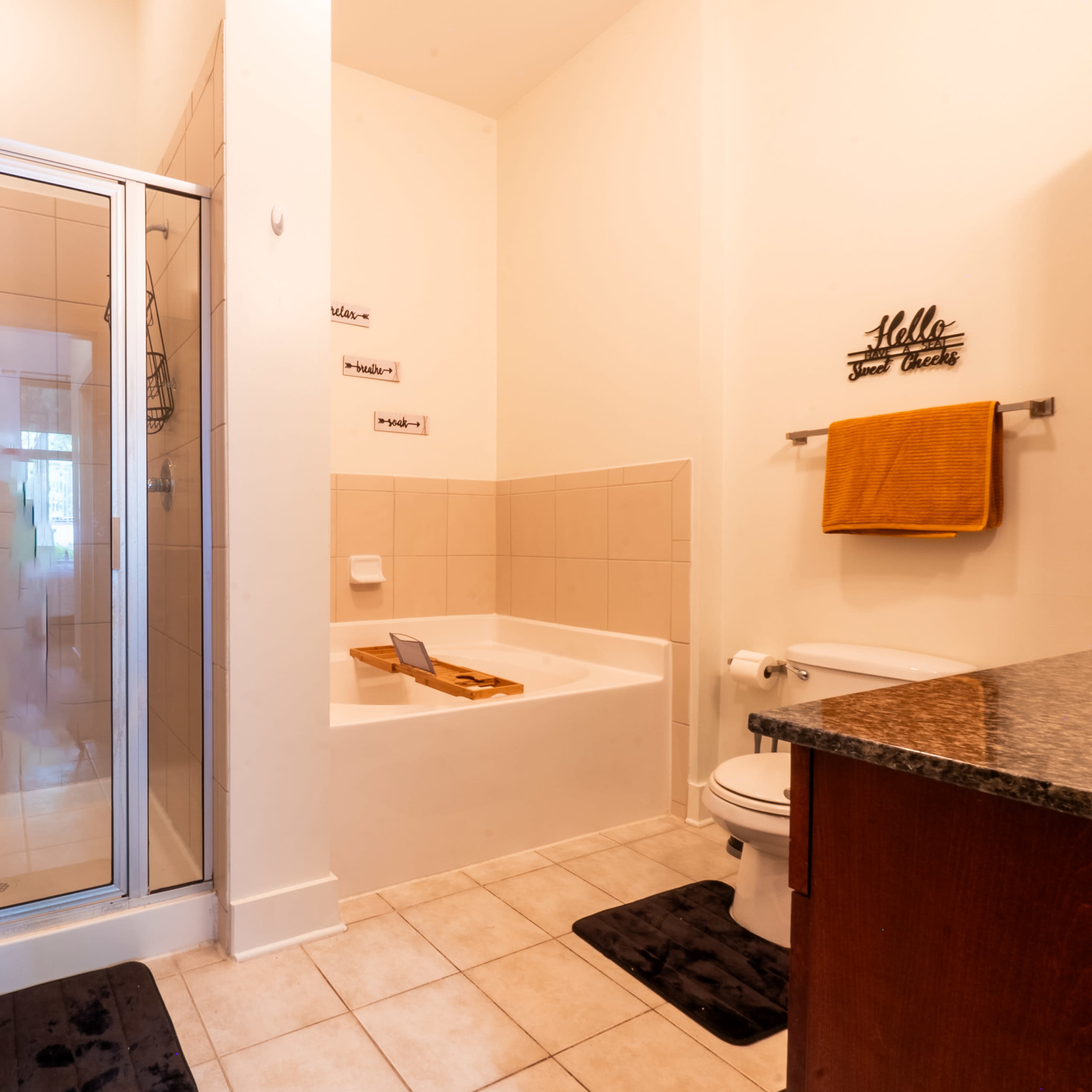 A bathroom featuring a glass shower stall, a separate bathtub with wooden accessories, a toilet, and a granite countertop with towels.
