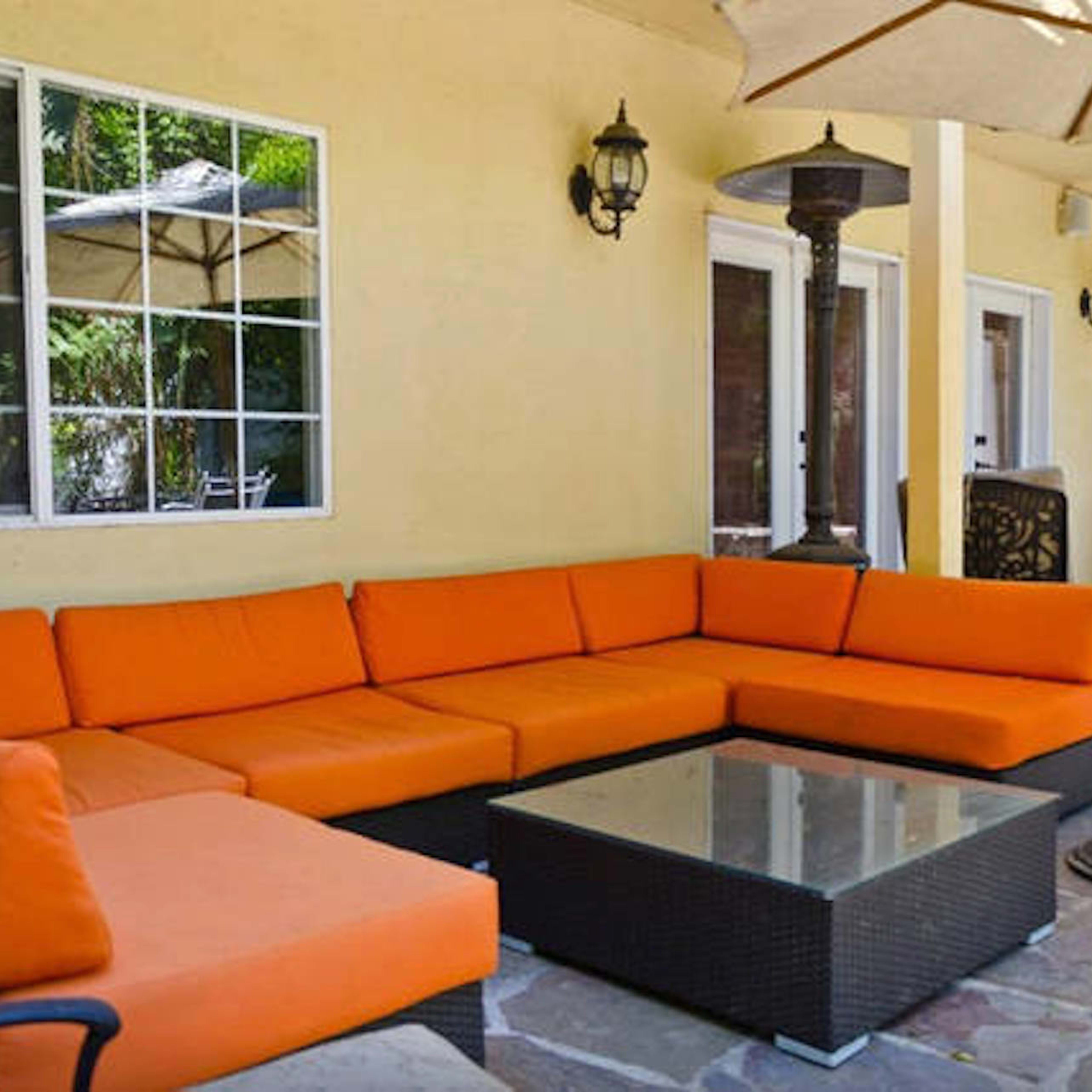 A large outdoor patio with a sectional orange sofa, a glass-top coffee table, and an umbrella providing shade.
