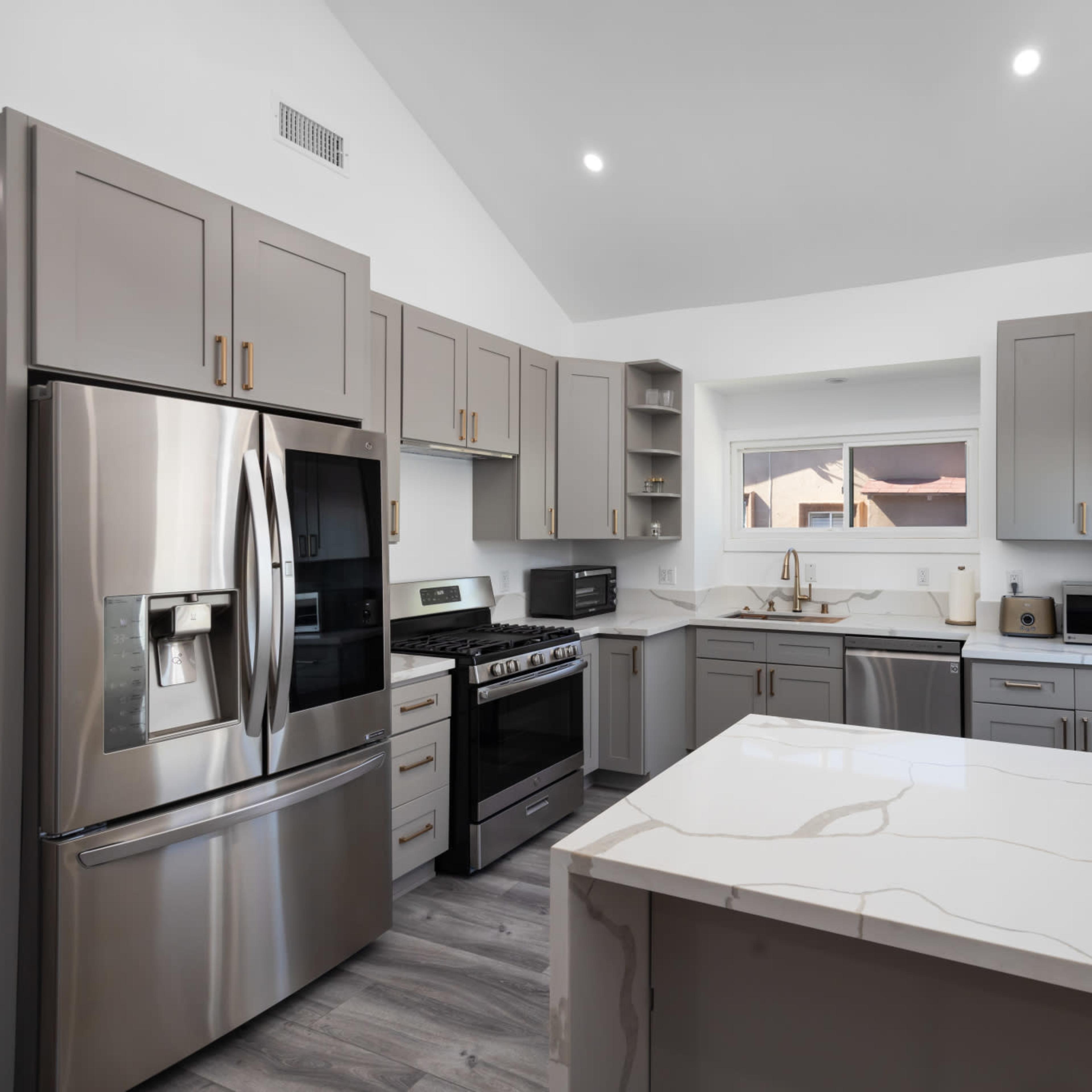 A modern kitchen with gray cabinets, stainless steel appliances, and a large island with a marble countertop.