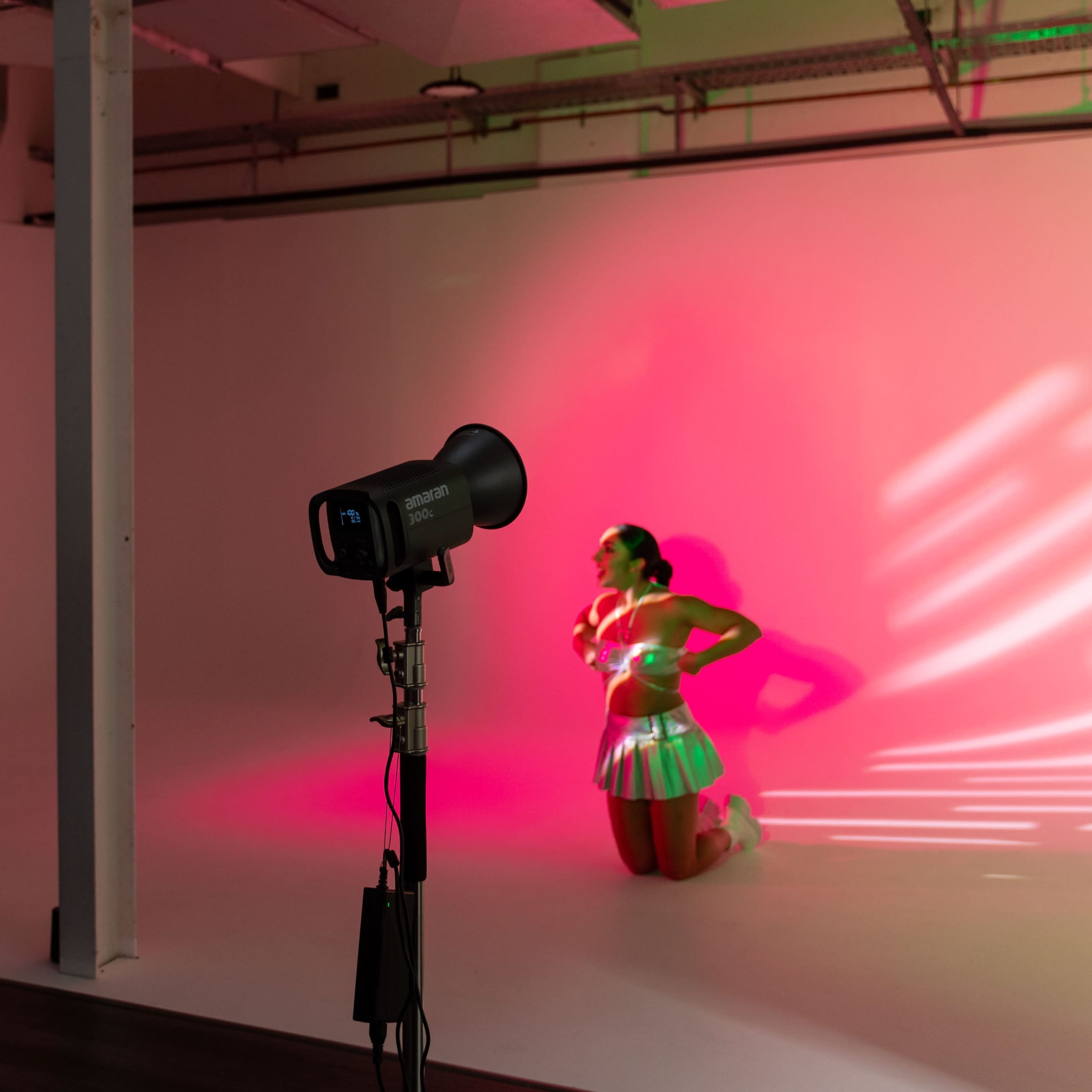 A model poses on a white backdrop while photographers and equipment are set up for a photoshoot.