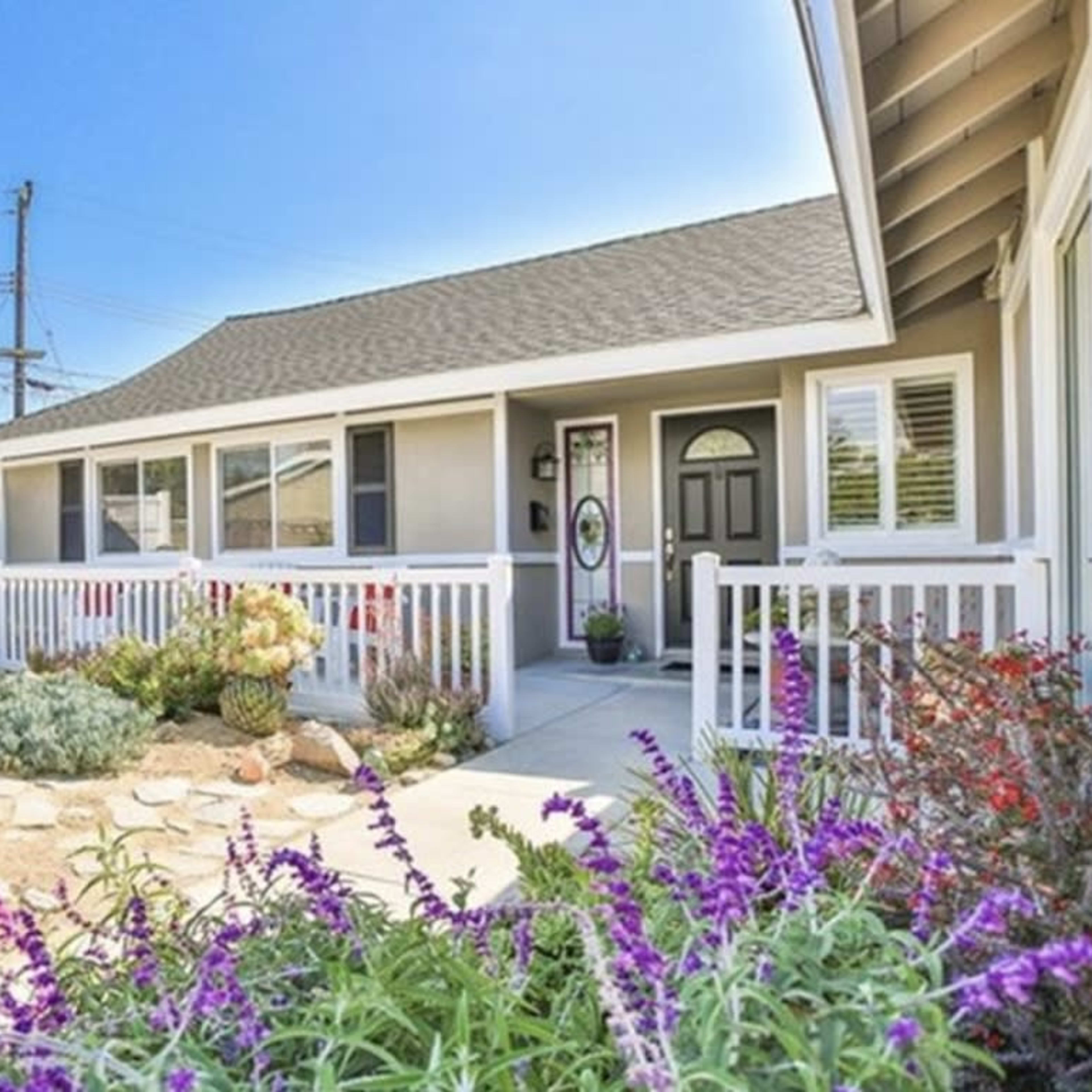 A residential house with a front yard featuring a pathway, various plants, and colorful flowers.