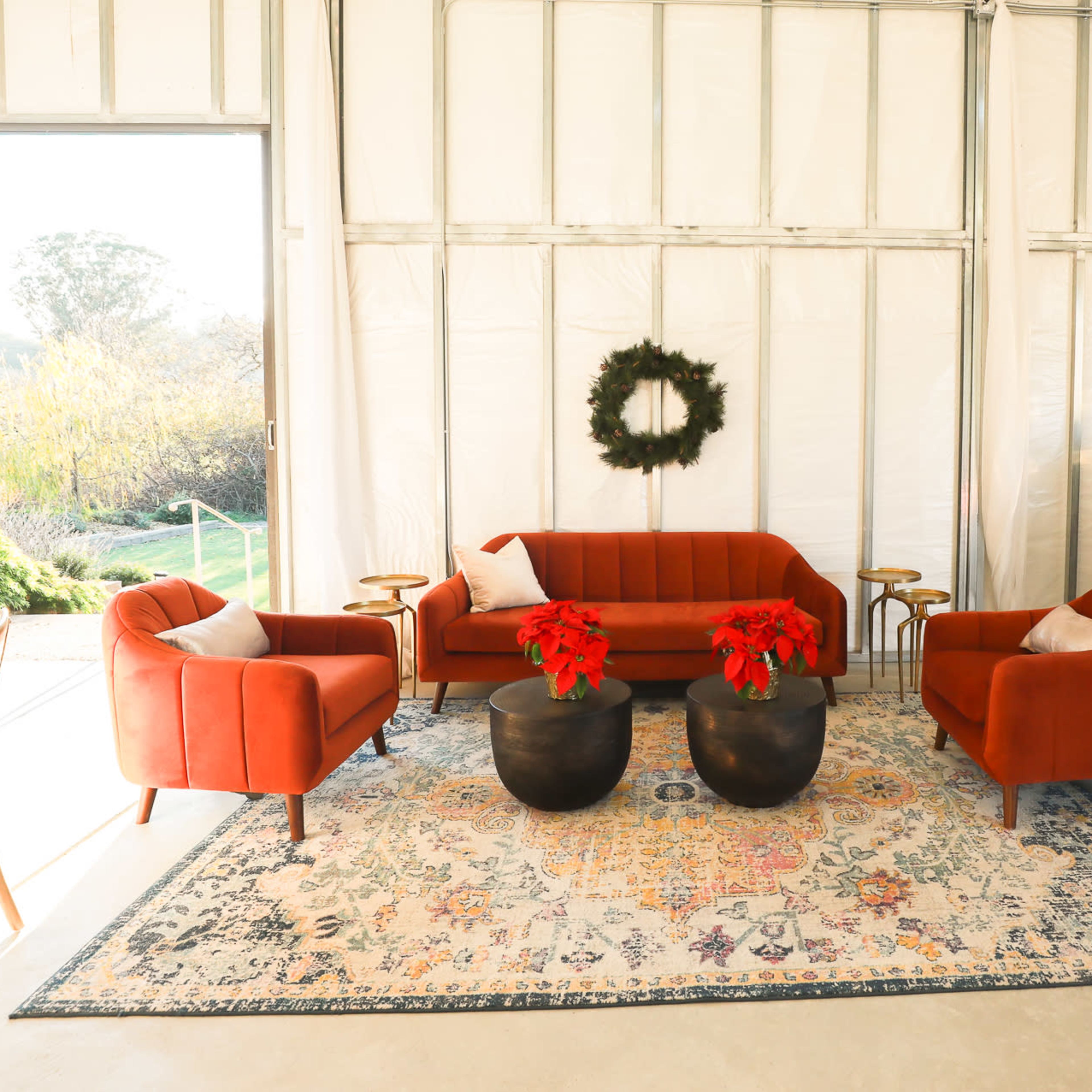 A modern lounge area features a red sofa and chairs around a patterned rug, with a black bar and festive decorations.