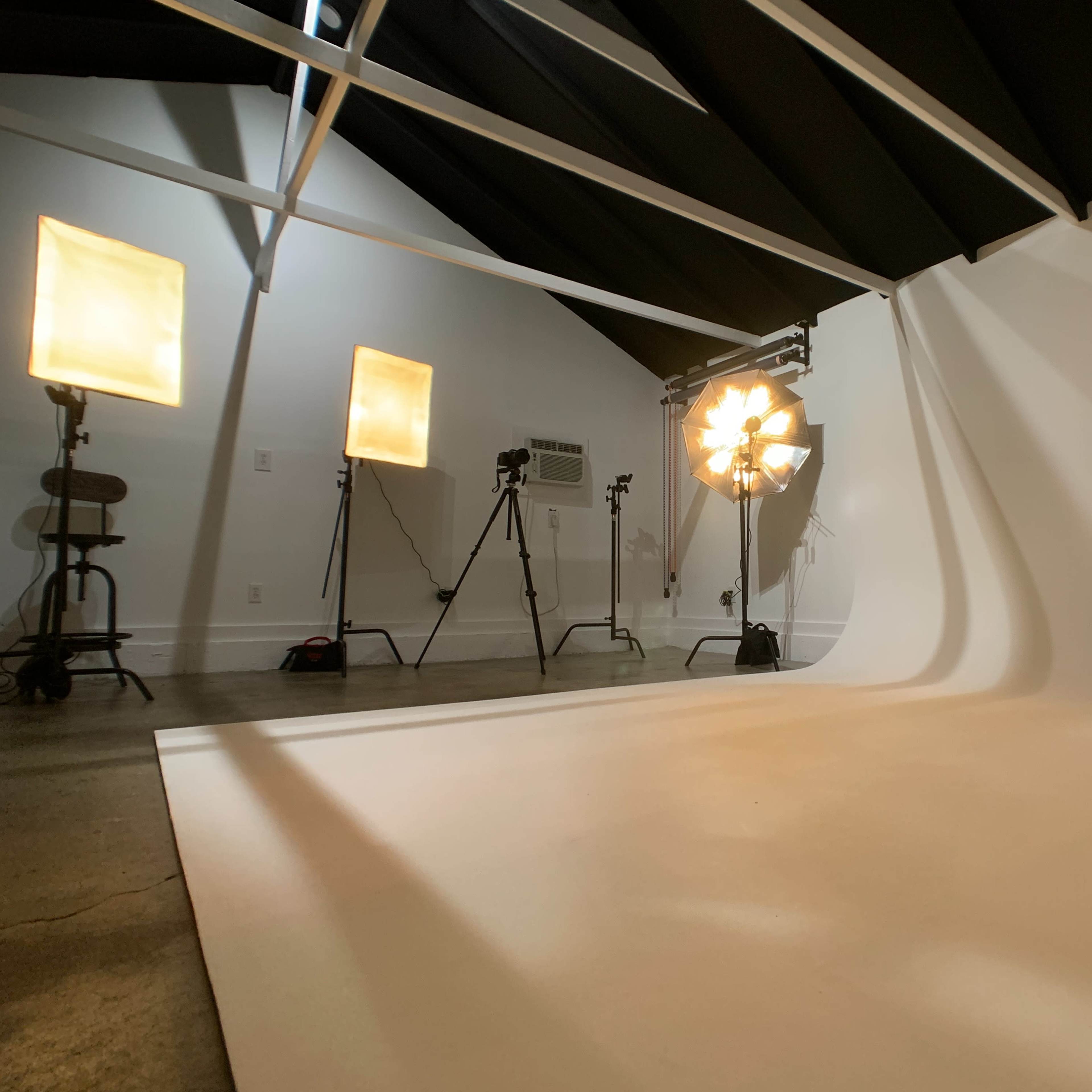 A photography studio with softbox lights and a backdrop set against a plain wall.