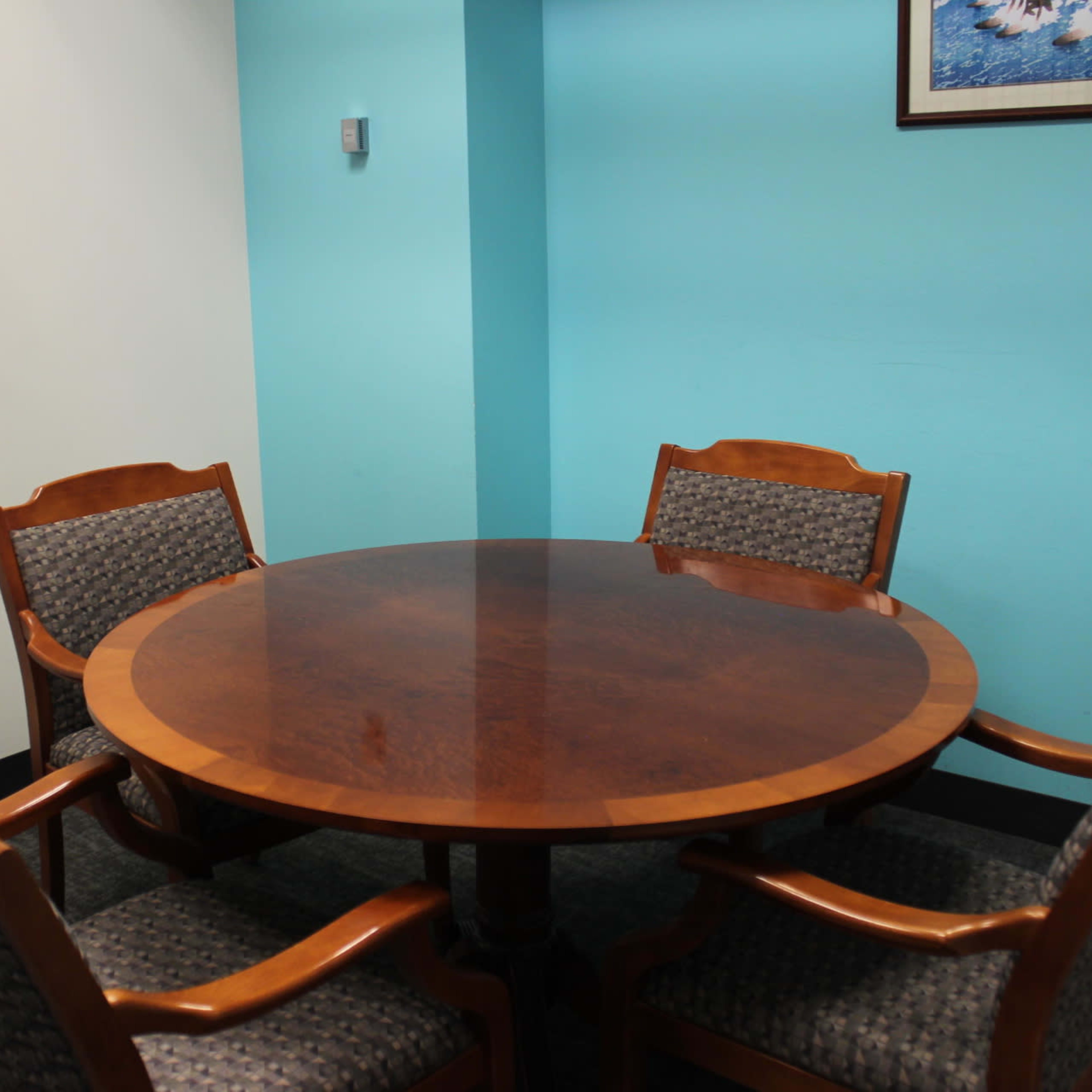 A round wooden table is surrounded by four upholstered chairs in a room with turquoise walls.