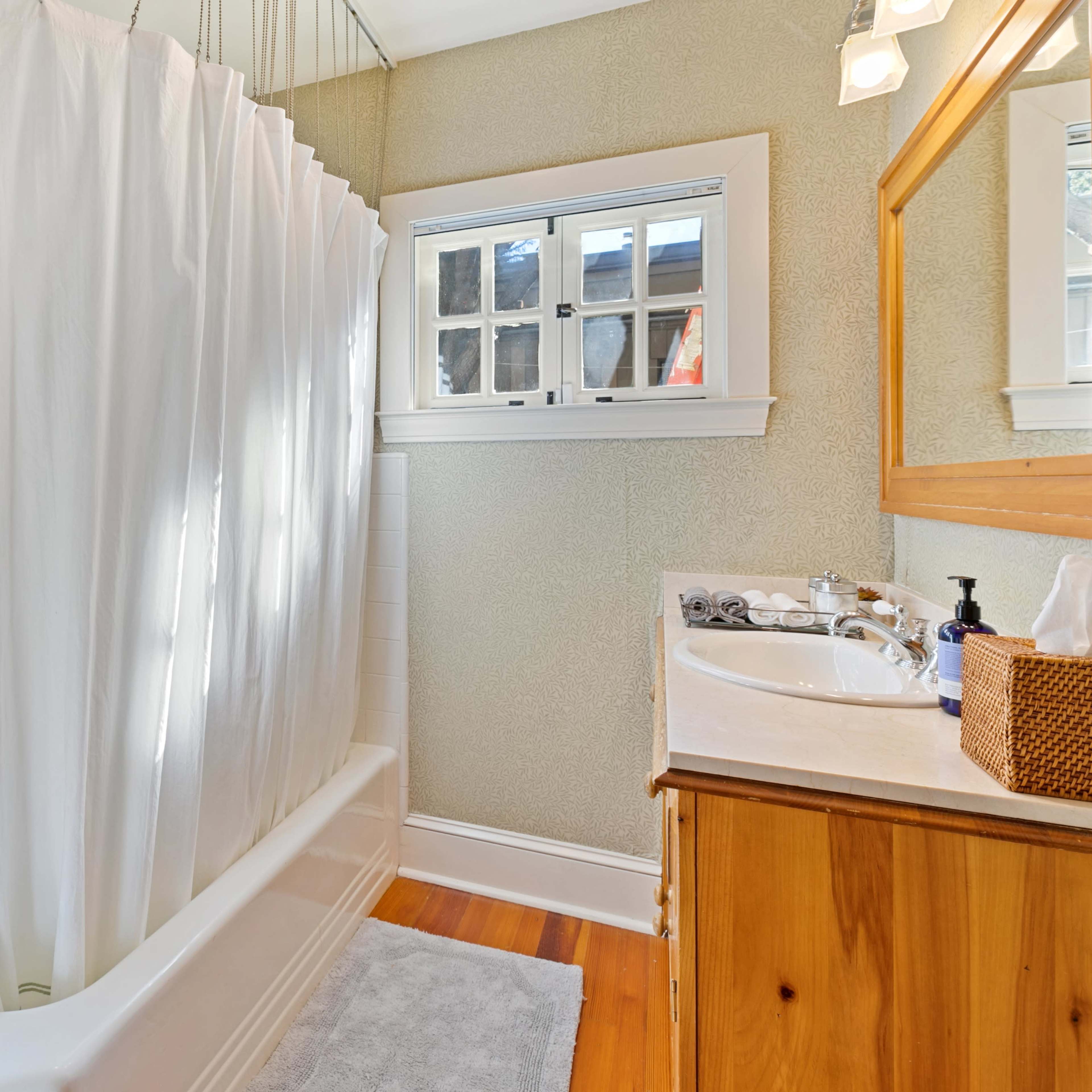 A bathroom featuring a white shower curtain, a bathtub, a window with multiple panes, and a wooden vanity with a mirror.