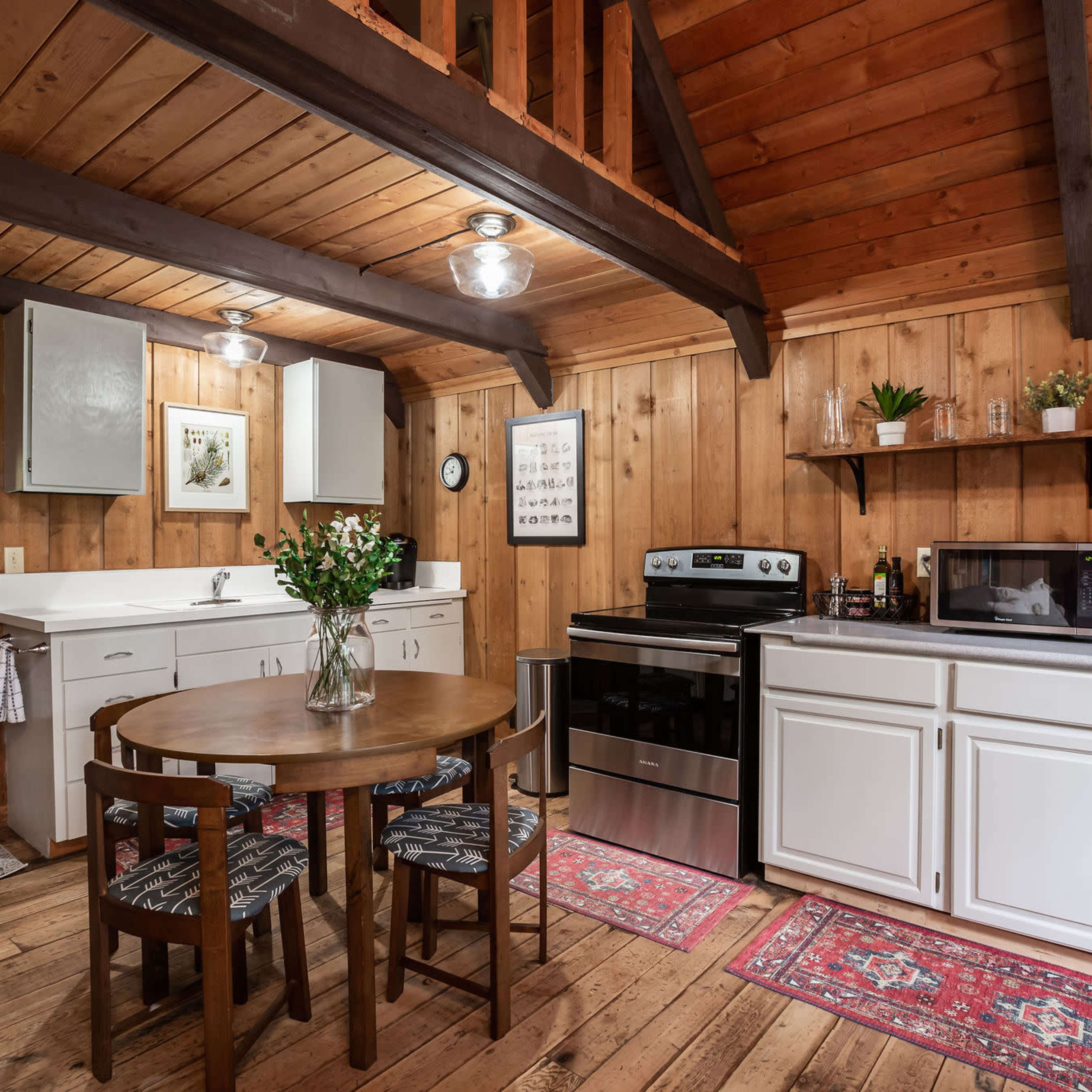 A rustic kitchen features wooden walls, a round table, and modern appliances amidst a cozy interior.