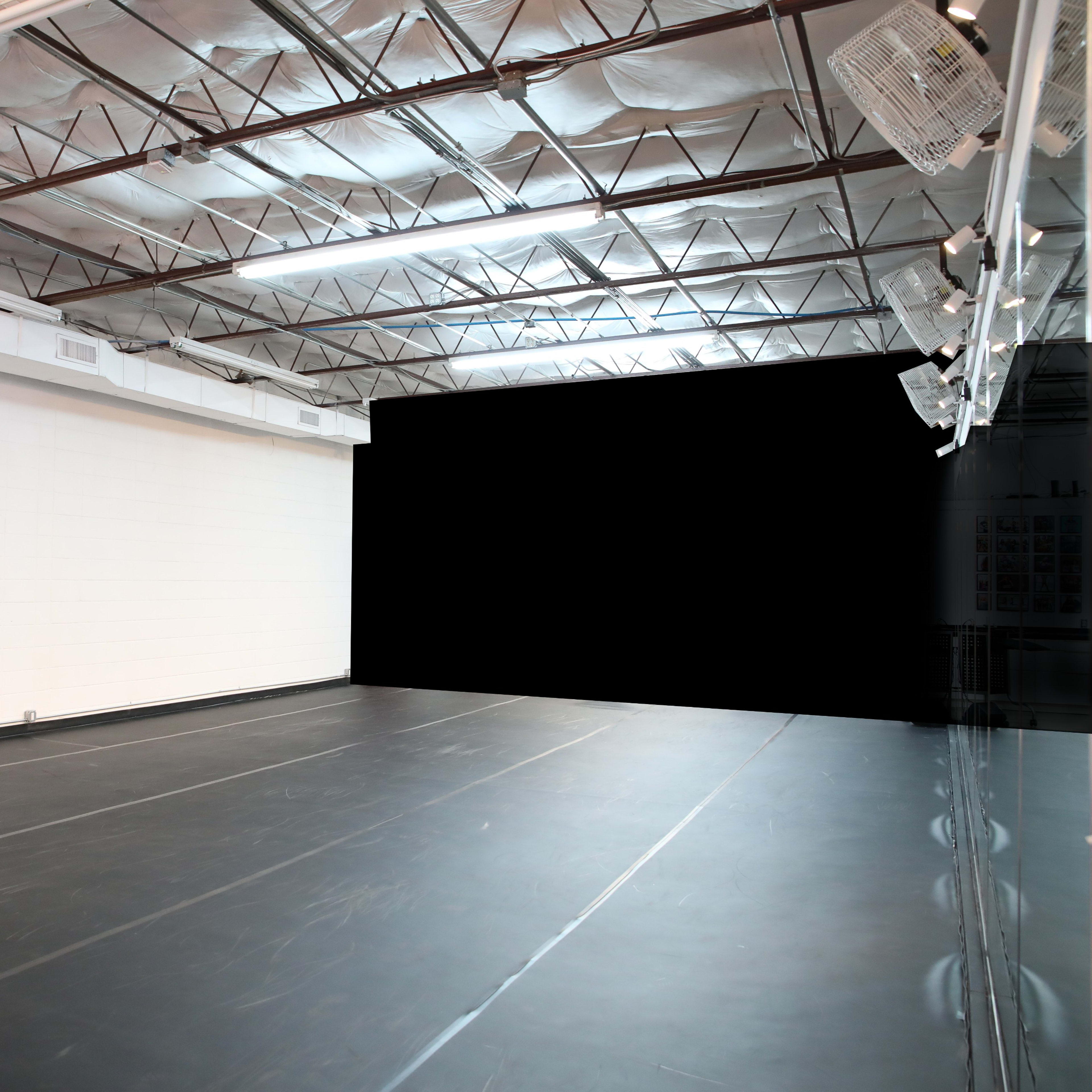An empty dance studio with a black floor and white walls illuminated by overhead lights.