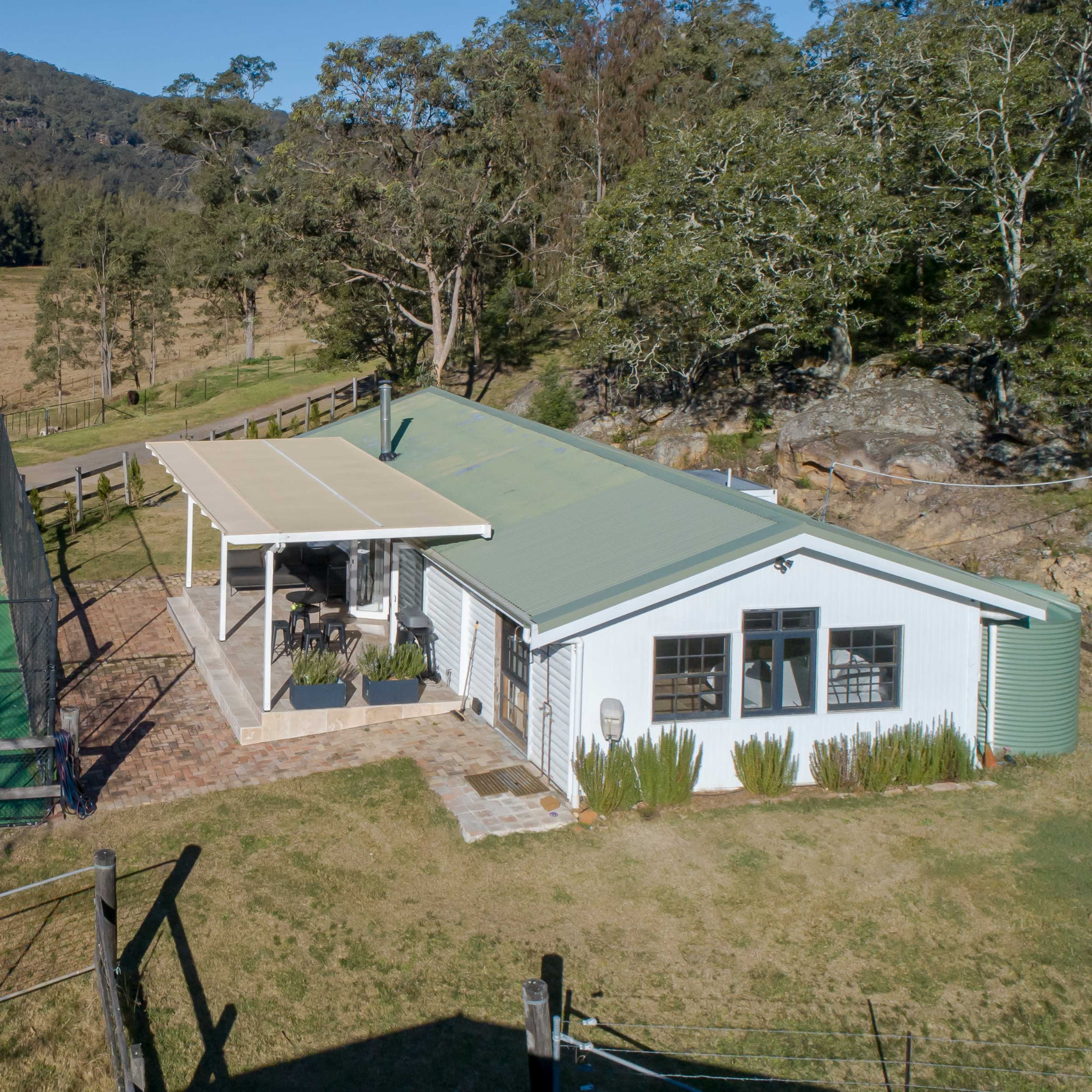 A small building adjacent to a tennis court surrounded by trees and open land.