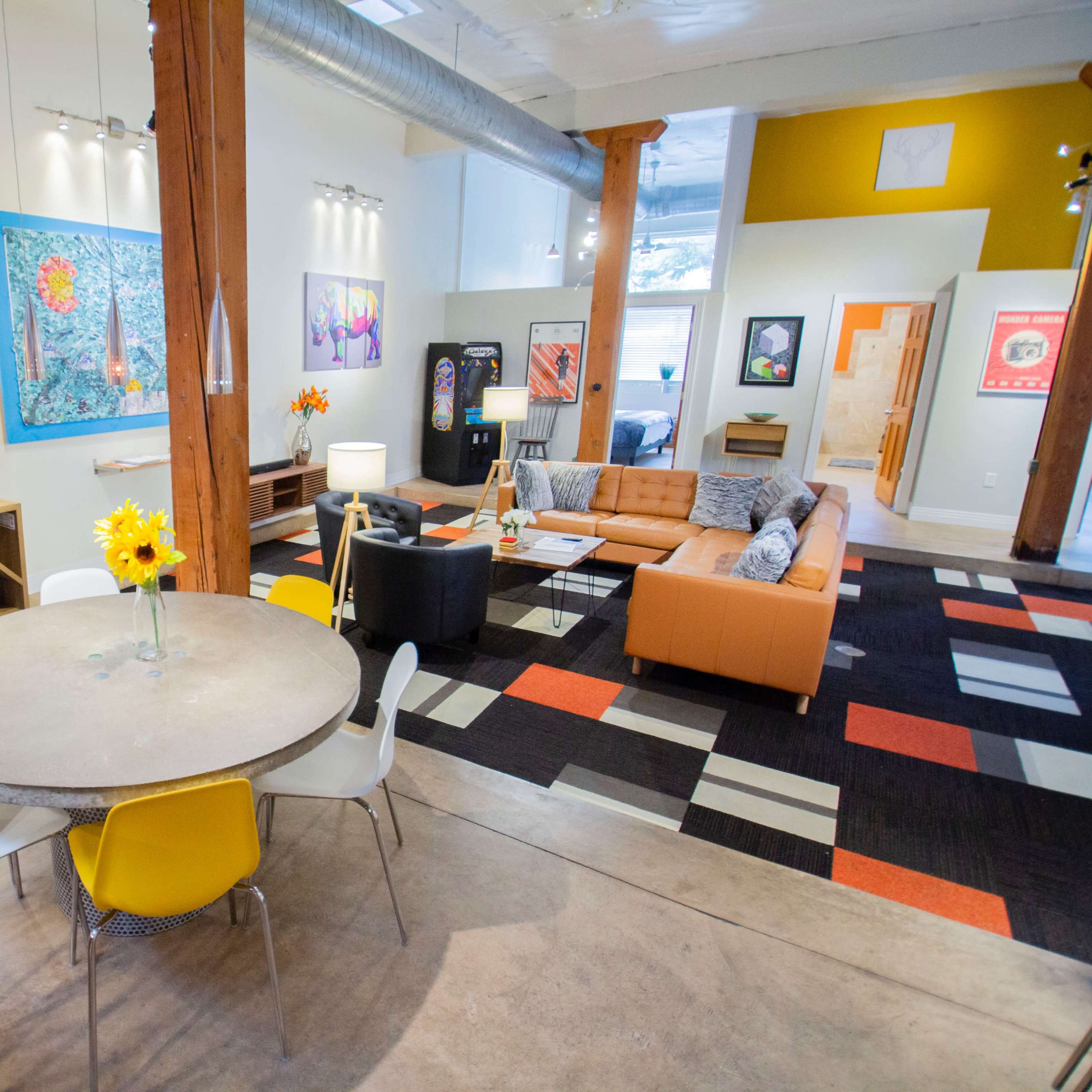 A spacious, modern living area featuring a circular dining table, an orange couch, and various artworks on the walls.