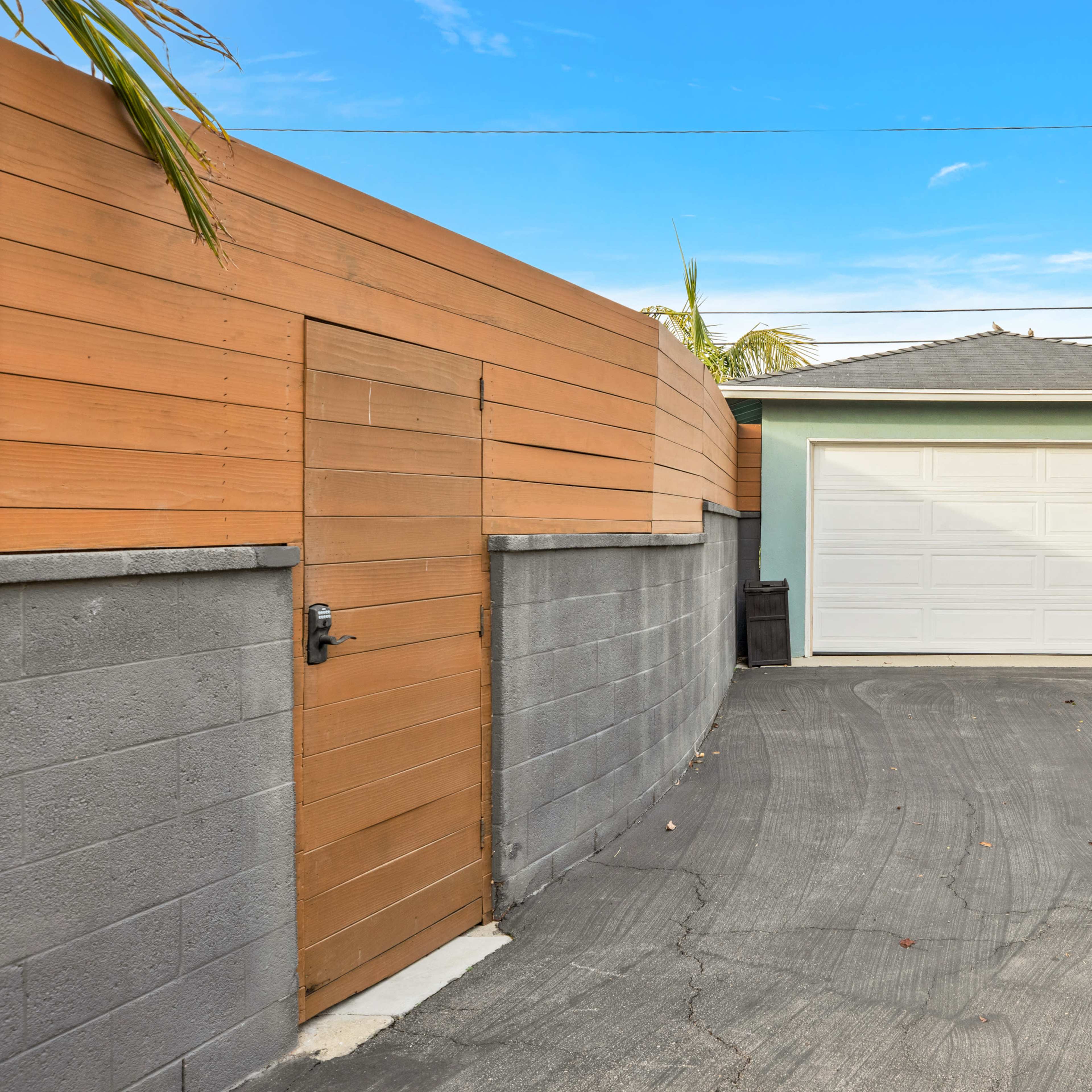 A driveway leading to a white garage door, bordered by wooden fencing and a concrete wall.