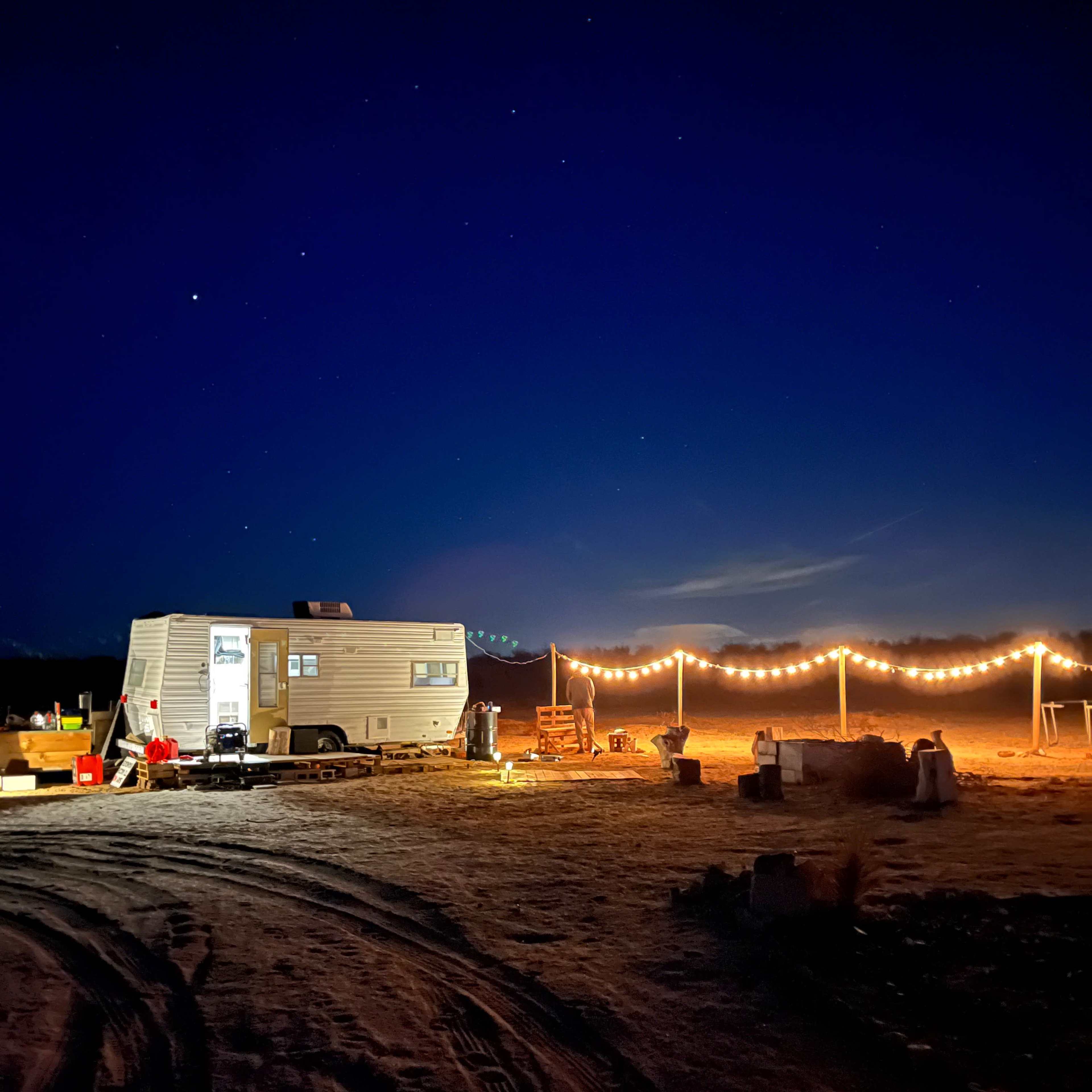 A trailer is set up in a dark, open area, illuminated by string lights against a starry night sky.