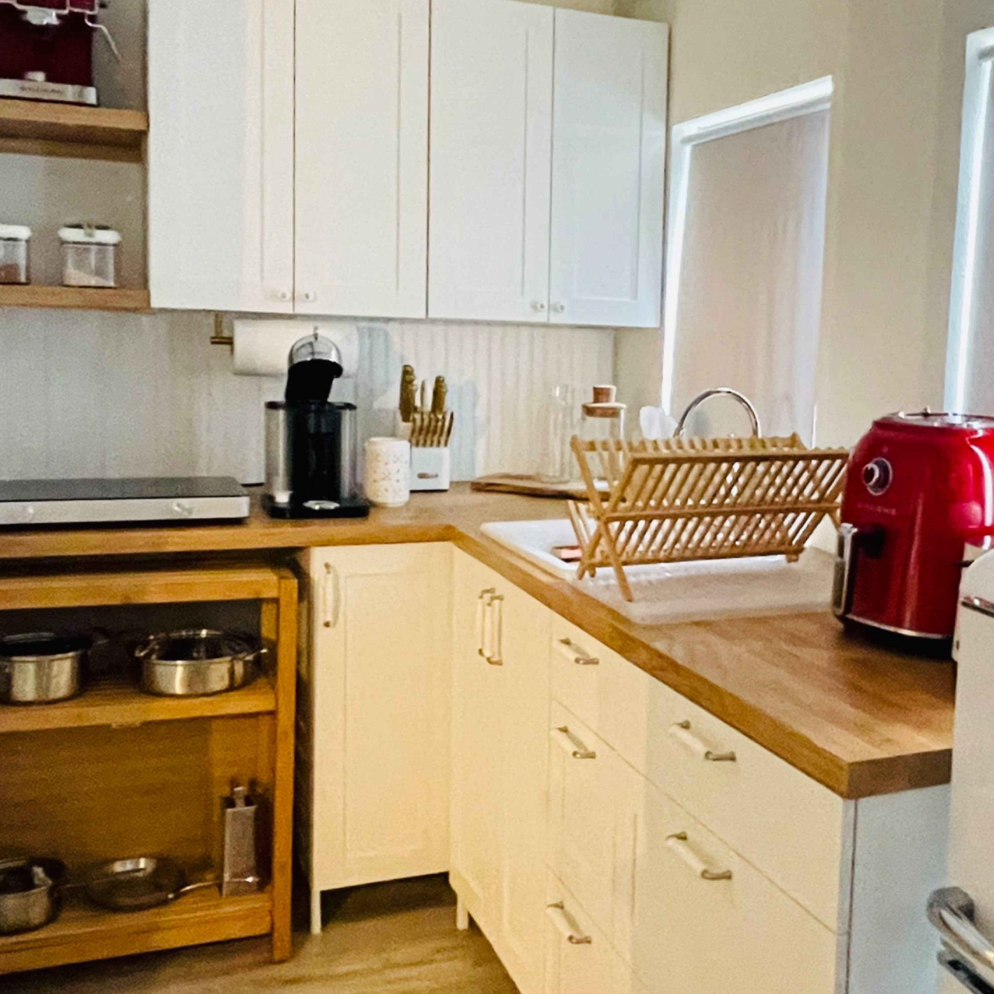 A bright kitchen with white cabinets, a wooden countertop, a red countertop appliance, and a vintage-style refrigerator.
