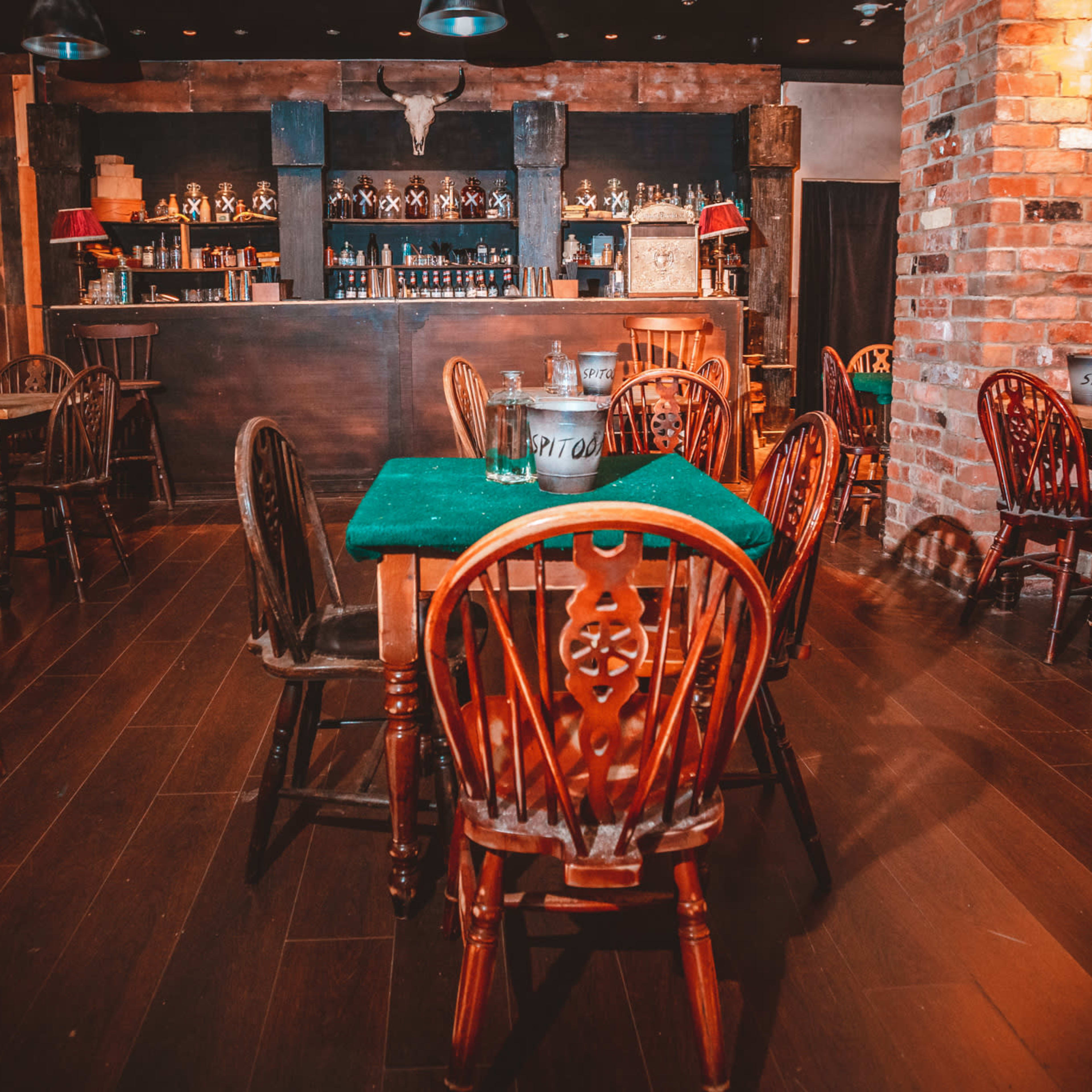 A rustic restaurant interior with wooden tables and chairs arranged around a bar in the background.