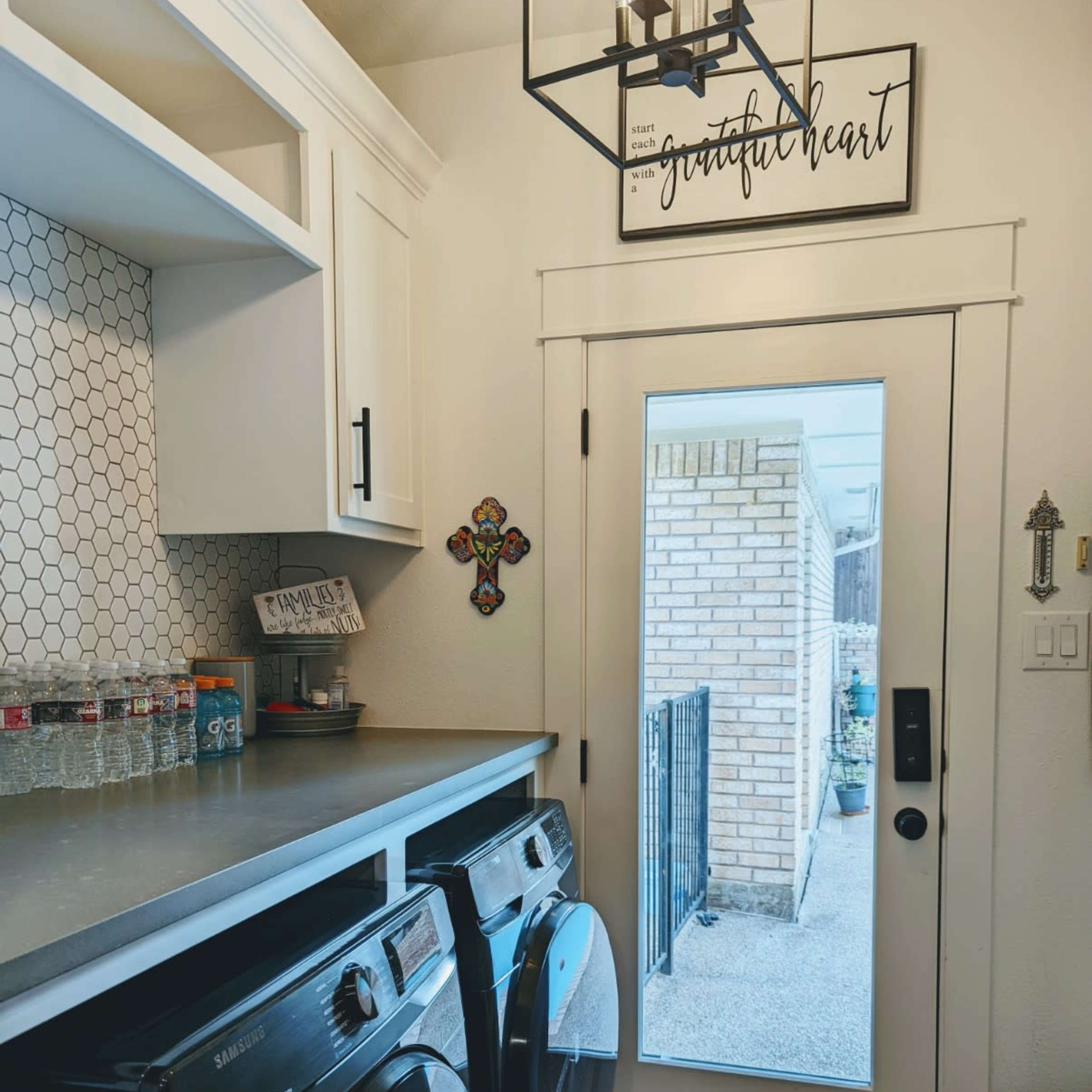 A laundry room features black washing machines, a countertop, and a door leading outside, with decorative elements on the wall.