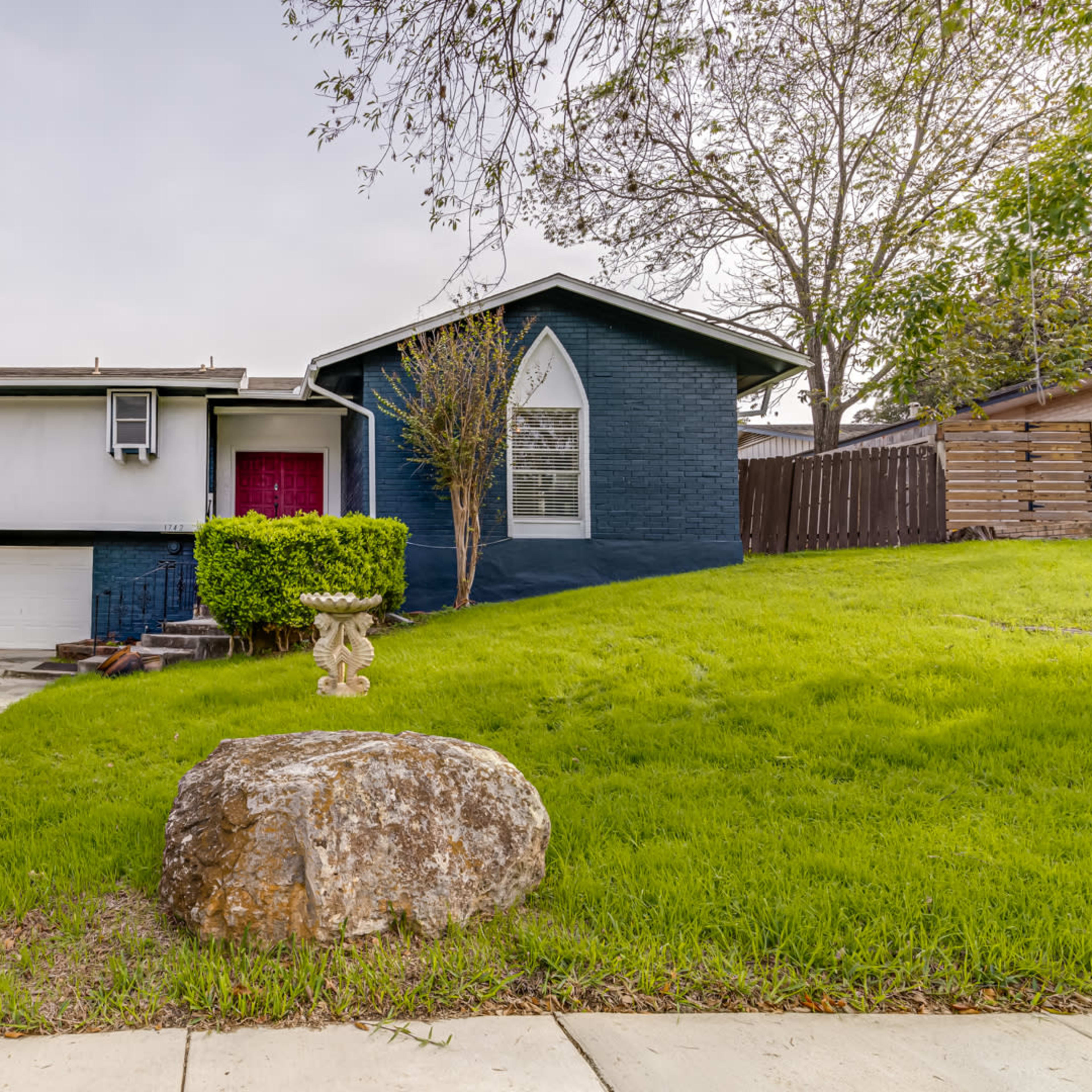 A single-story house with a split facade, featuring a blue and white exterior, a front lawn, and a large rock in the foreground.