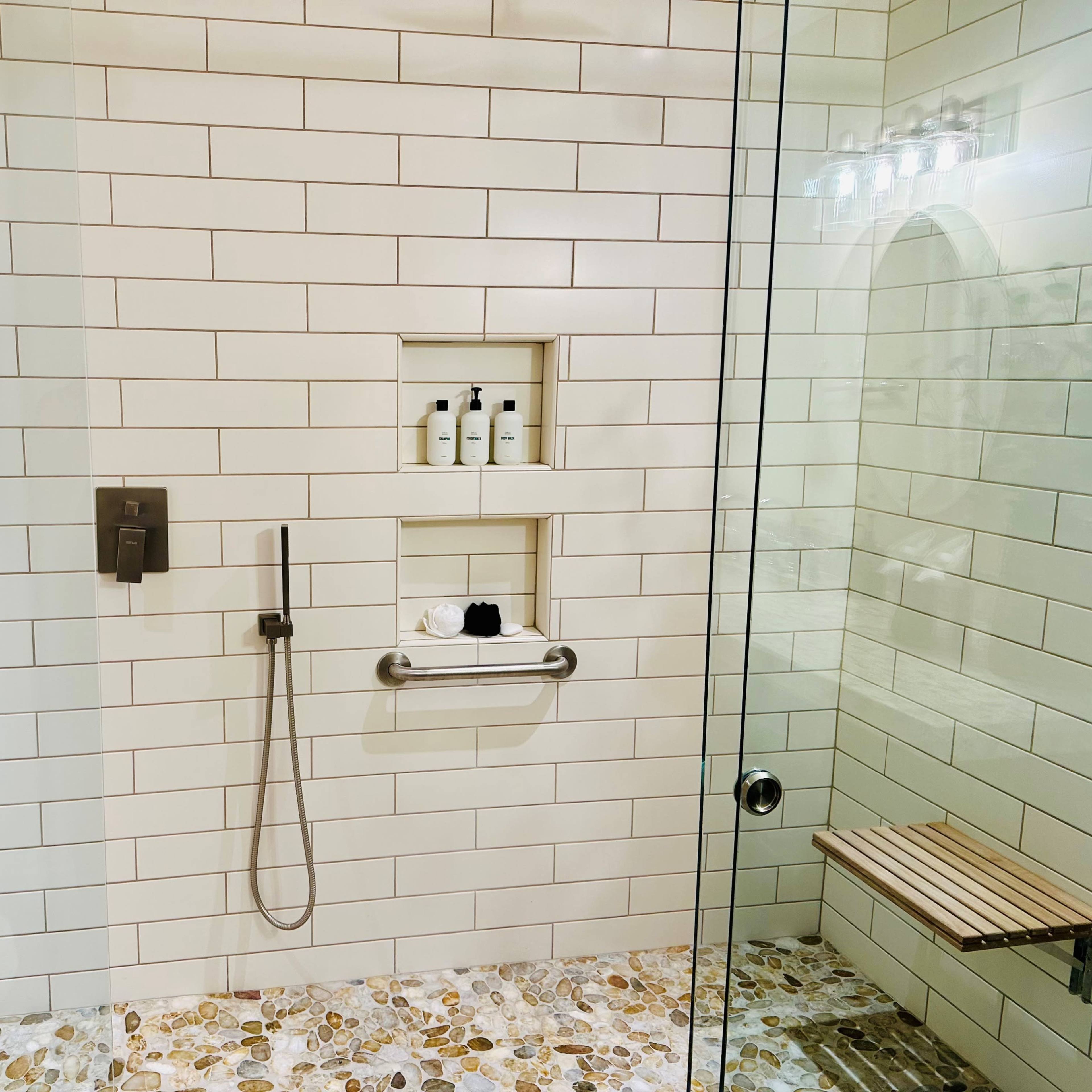 A modern shower with white tiled walls, a glass door, and a built-in shelf displaying toiletries.