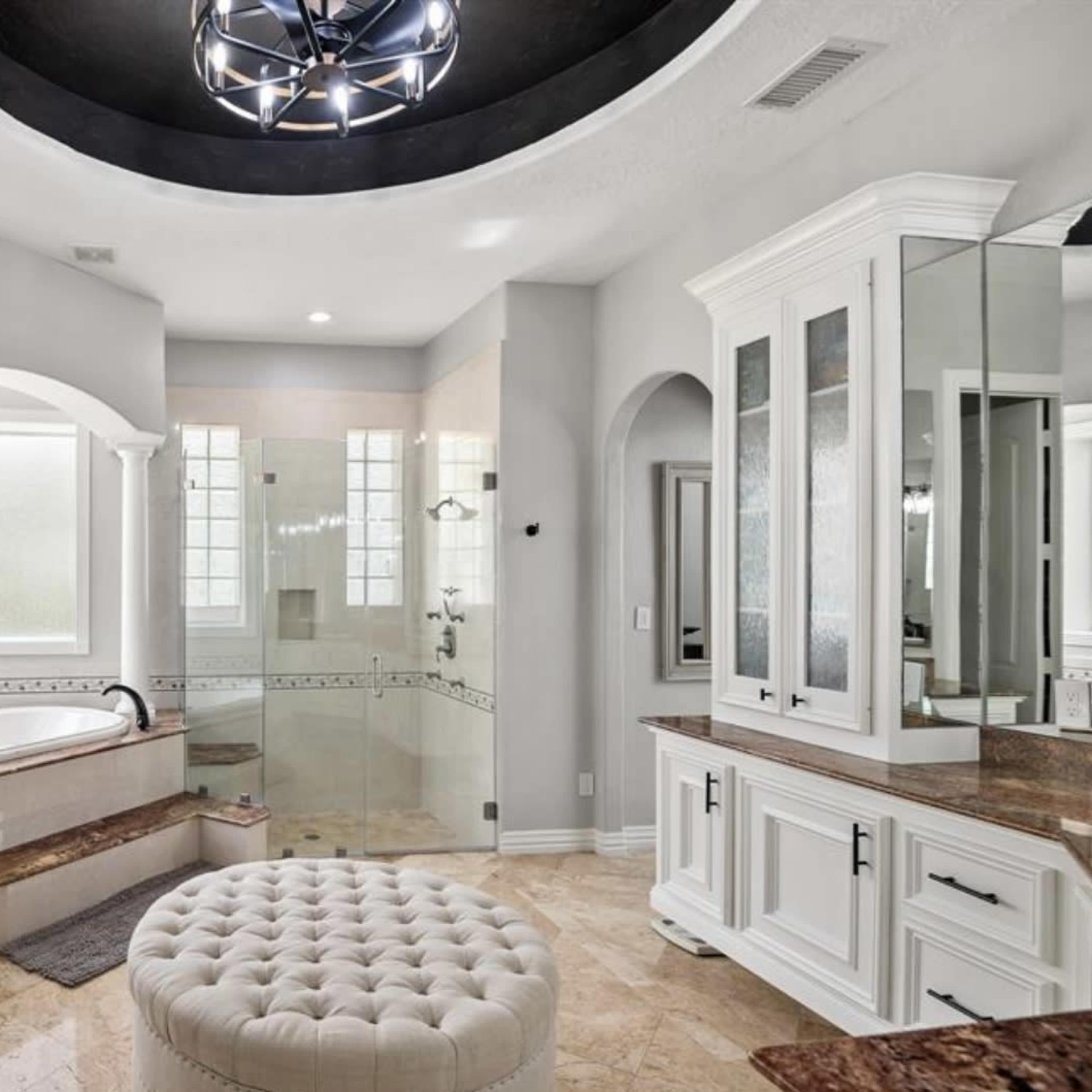 A modern bathroom featuring a large soaking tub, a glass shower enclosure, and dual vanities with white cabinetry and marble countertops.