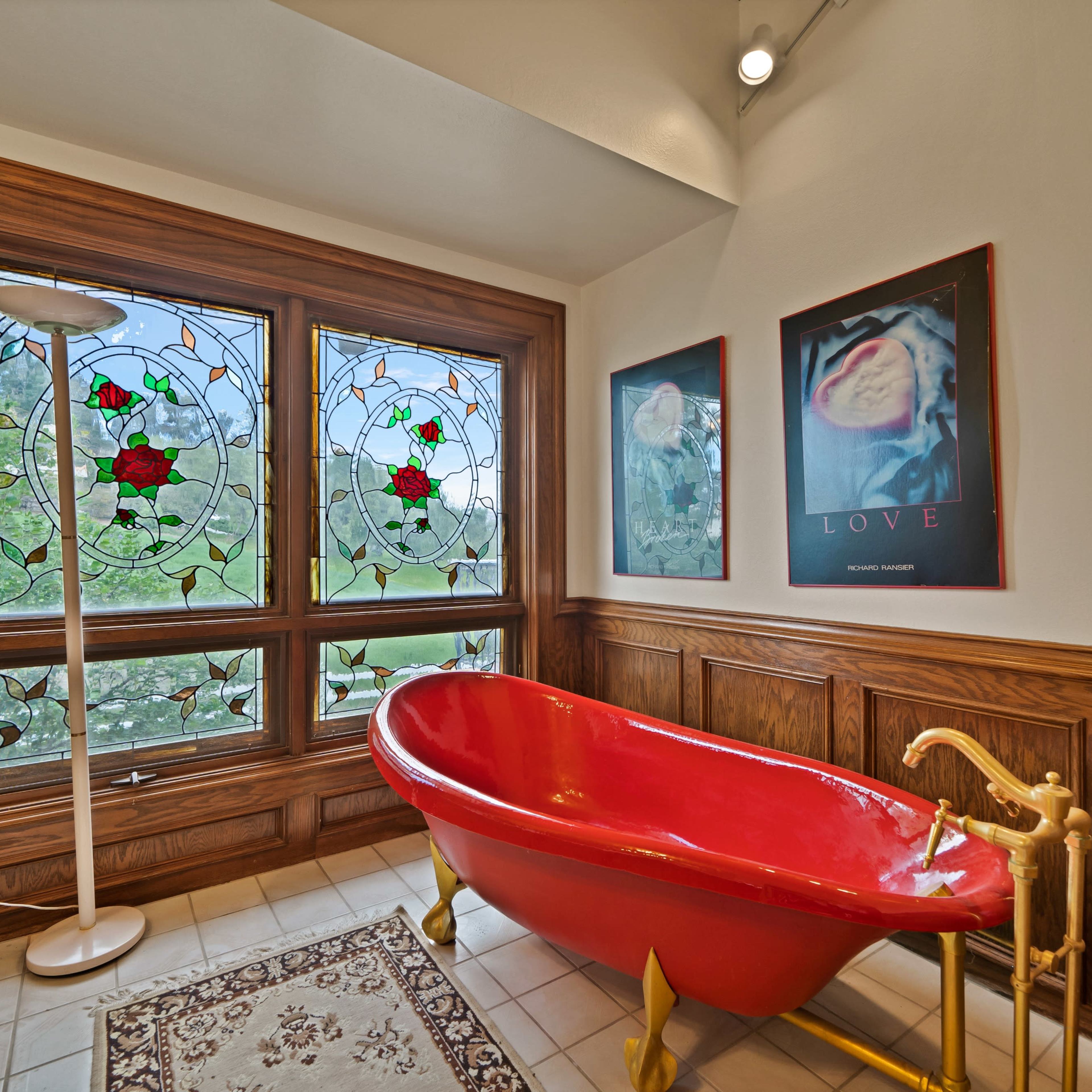 A red clawfoot bathtub in a room with stained glass windows and wooden paneling.