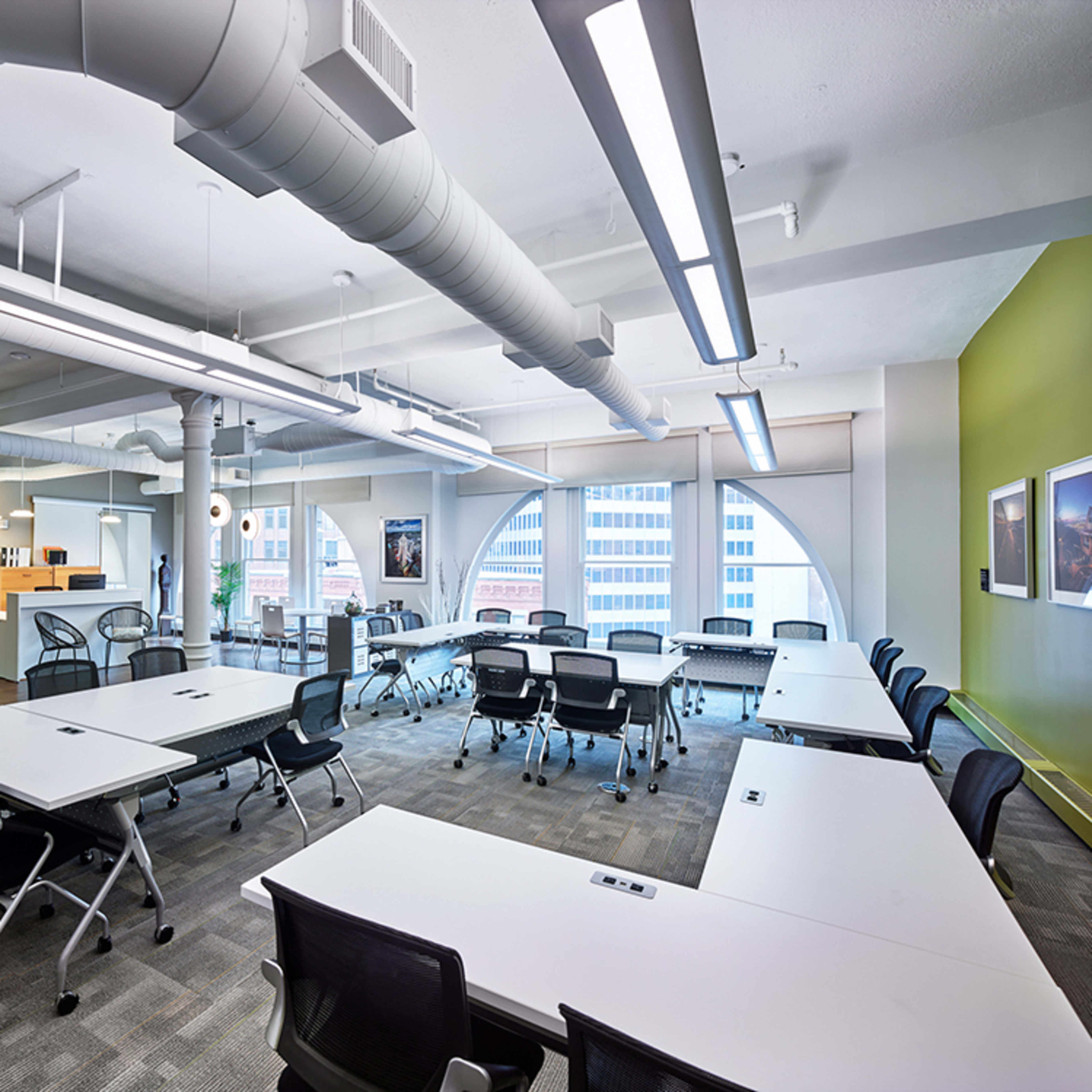 A modern office space with multiple tables arranged for meetings, surrounded by large windows and contemporary furnishings.