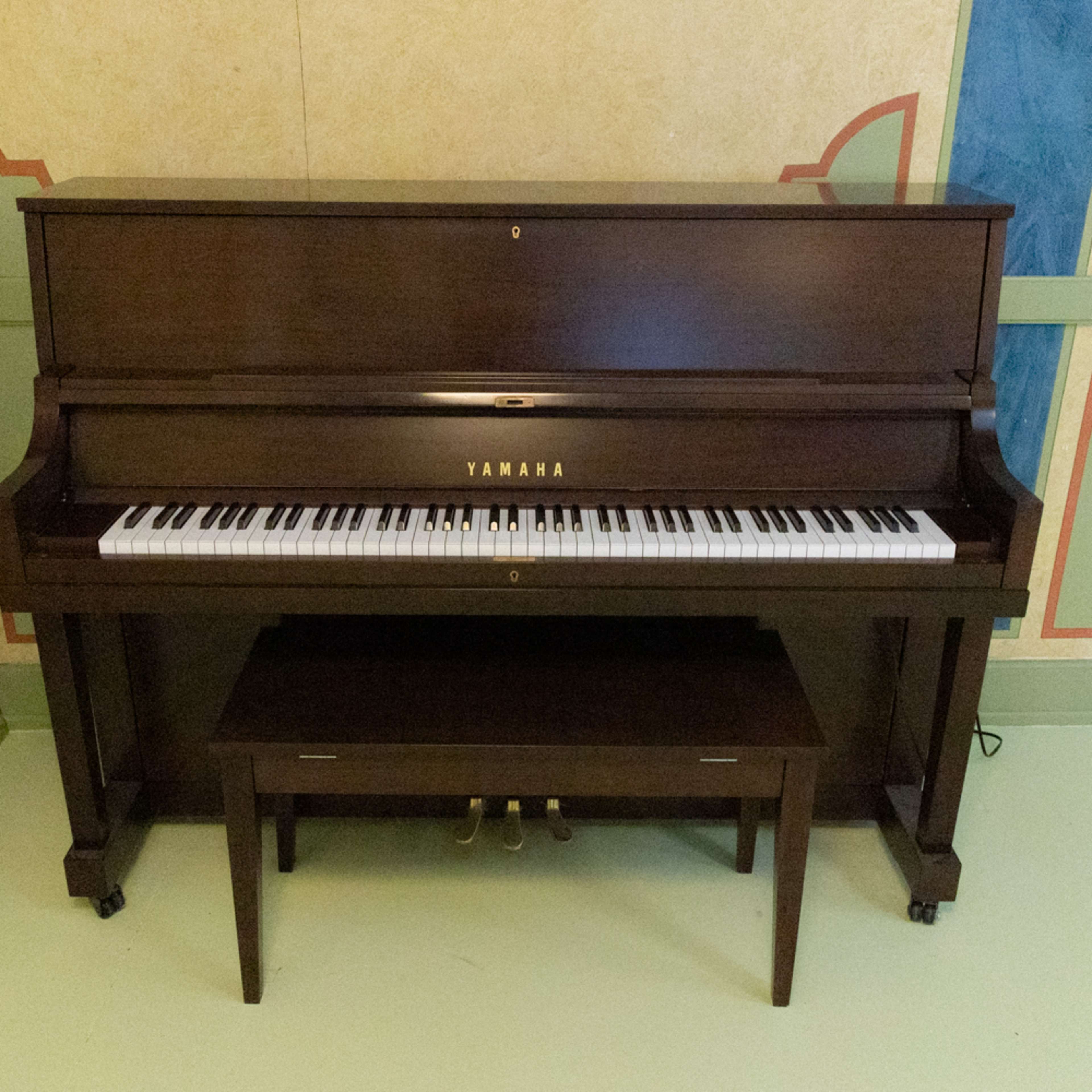 A Yamaha upright piano is positioned against a textured wall with decorative elements, complemented by a matching bench in front.