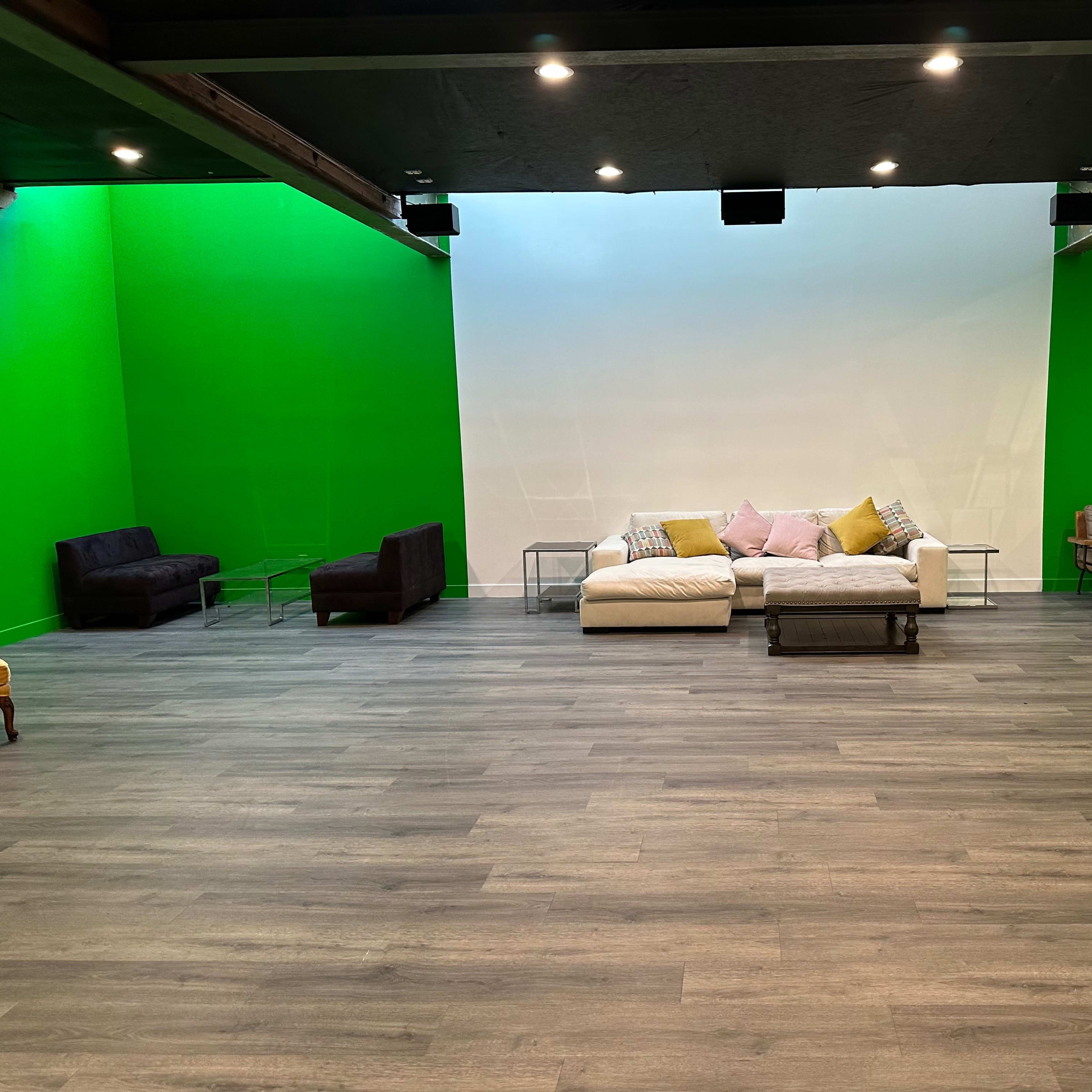 A room with a bright green wall, featuring various seating arrangements, including a white couch with decorative pillows, two armchairs, and a coffee table on a wooden floor.
