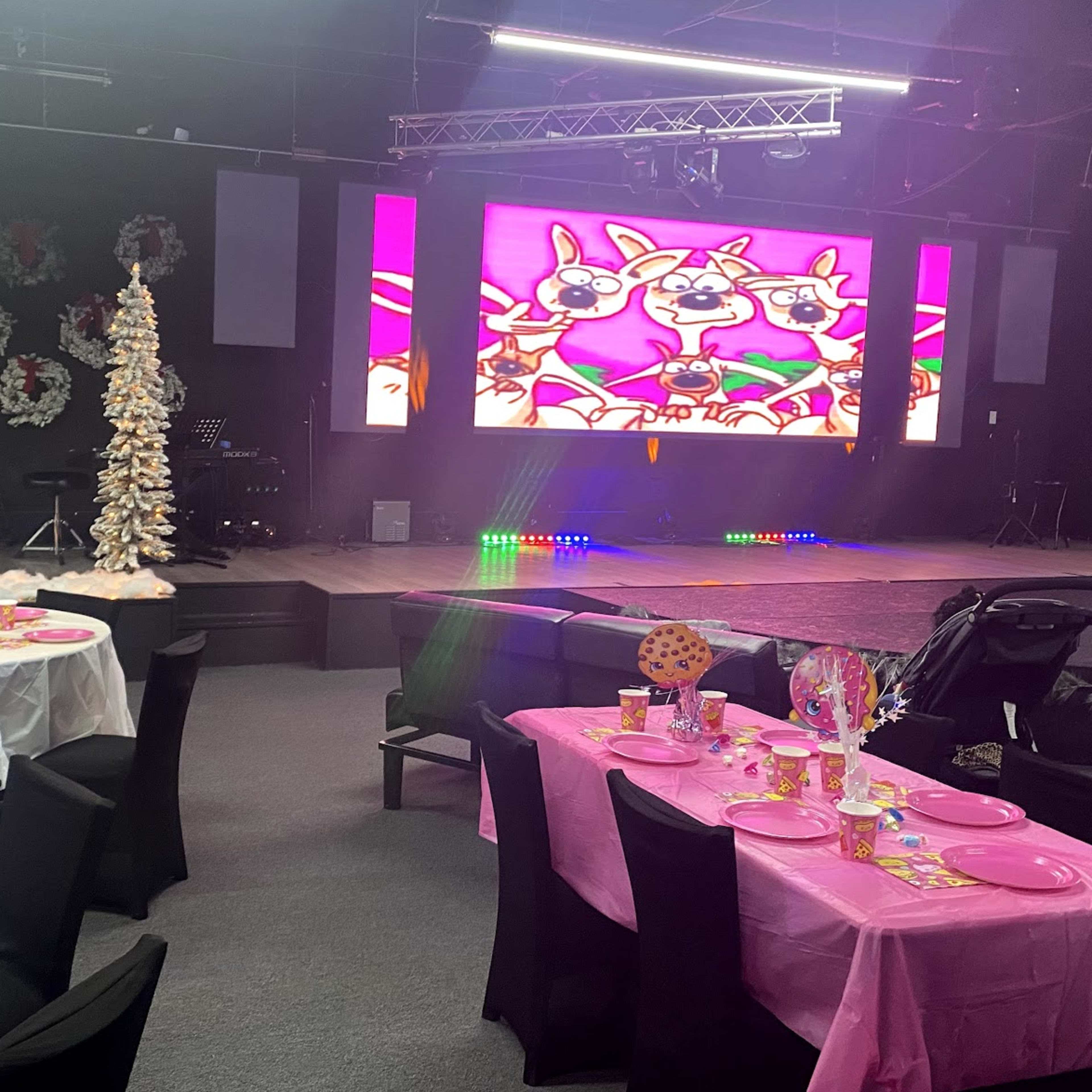 A decorated event space with tables set for a party, featuring colorful tableware and a backdrop displaying animated characters on a large screen.