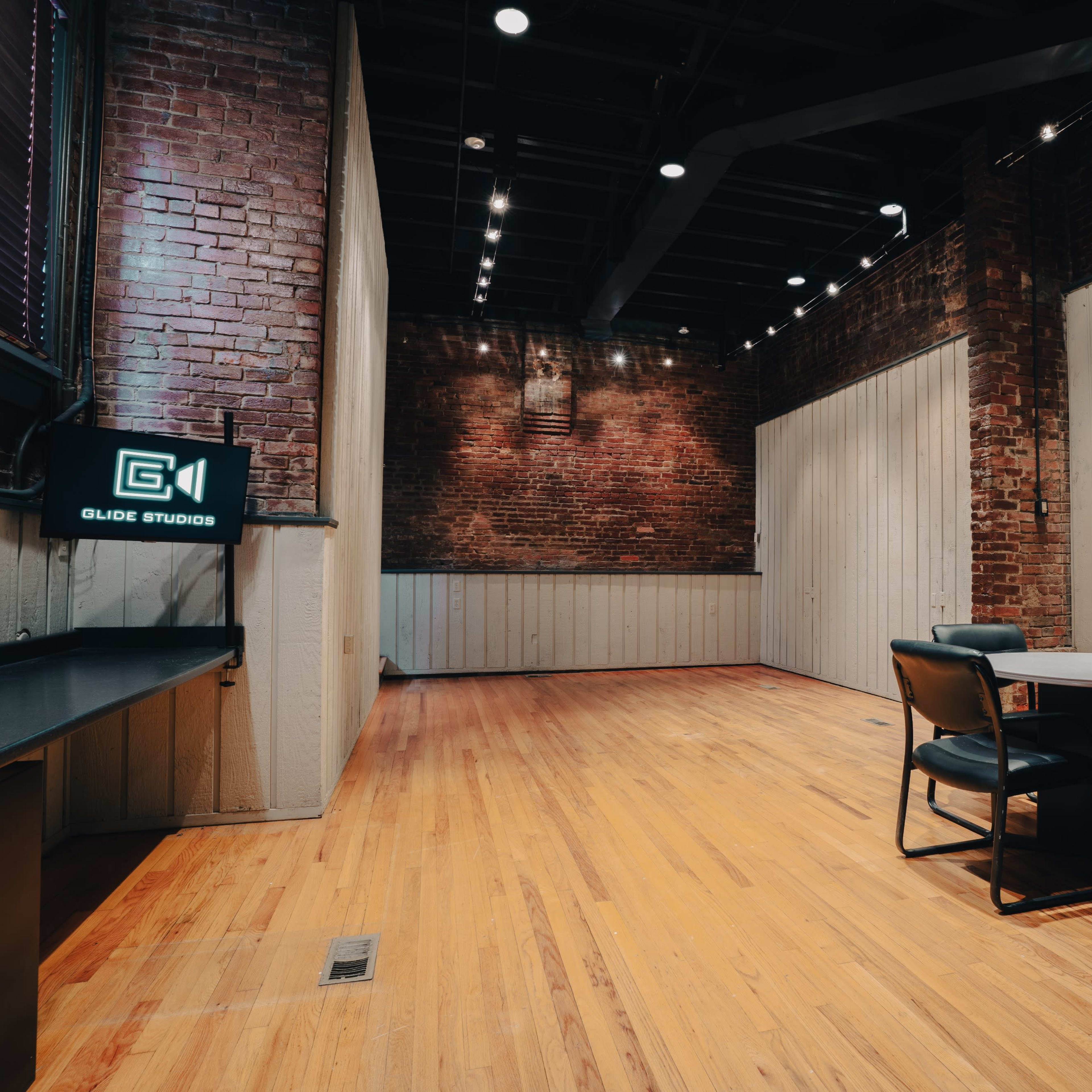 A spacious, empty studio with exposed brick walls, wooden flooring, and a round table with four chairs.