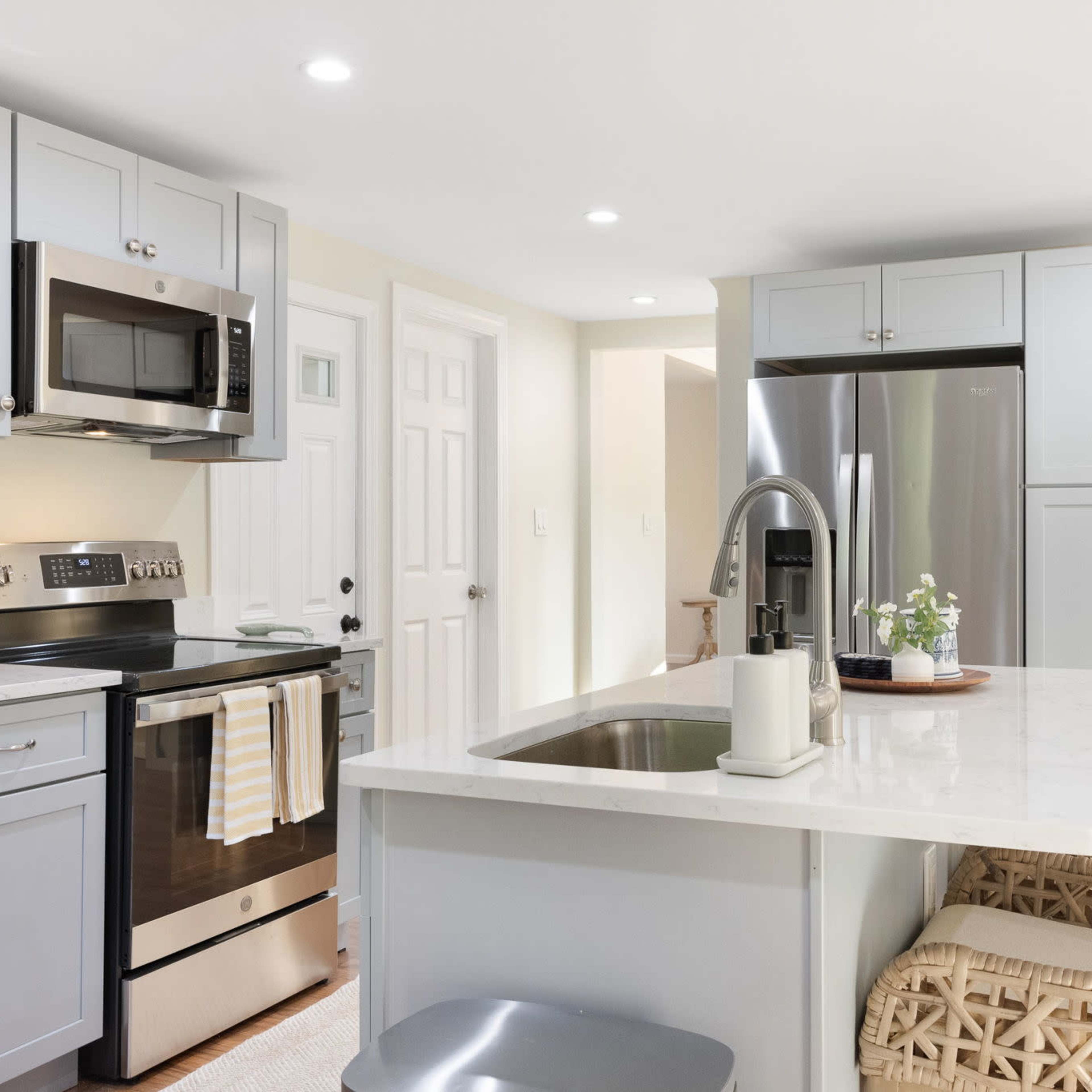 A modern kitchen features gray cabinets, stainless steel appliances, and a central island with woven bar stools.