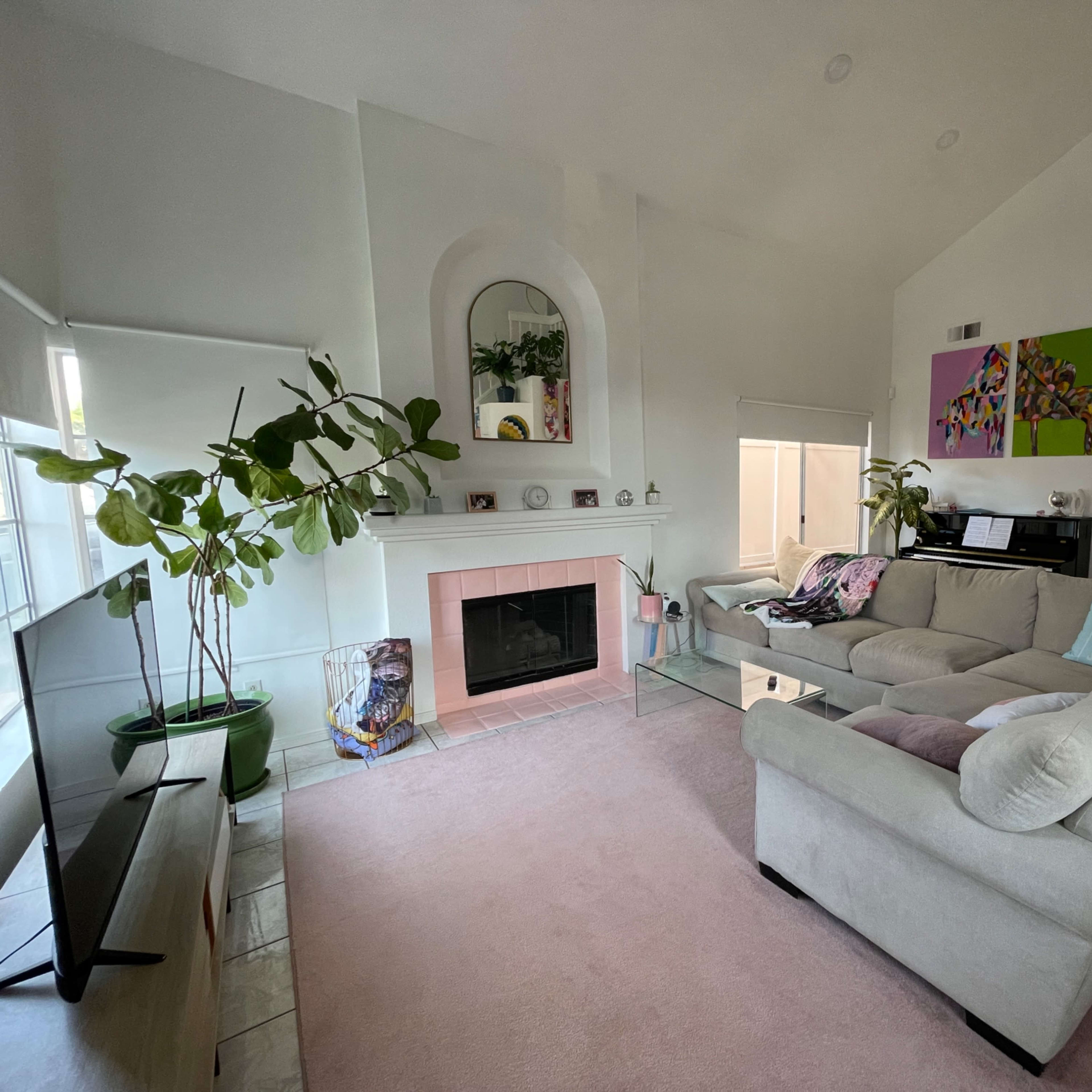The living room features a large beige sectional sofa, a fireplace with a pink surround, and large windows allowing natural light to fill the space.