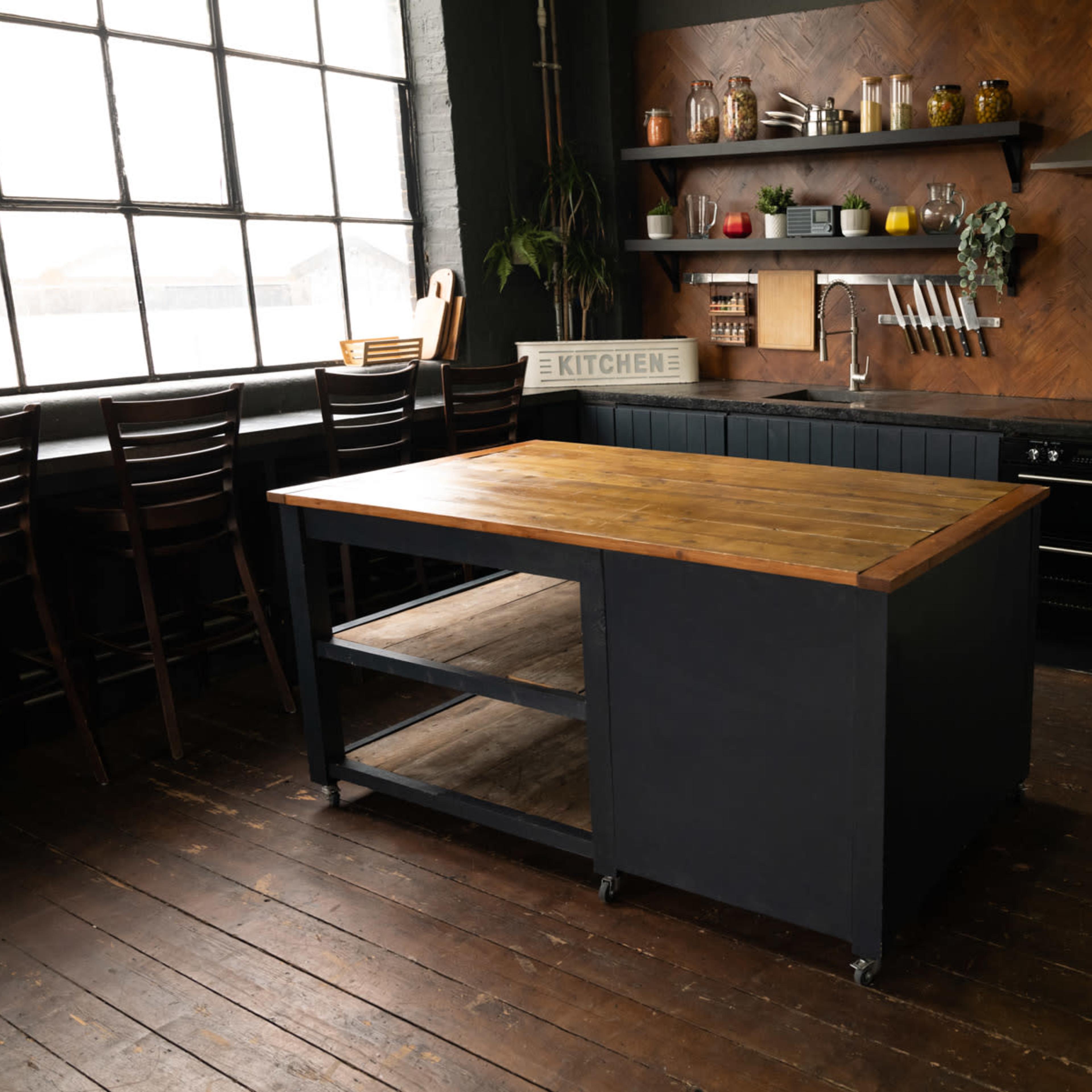 A modern kitchen featuring a wooden island with a dark base, black cabinets, and a vintage-style refrigerator, all set against a backdrop of a large window and wooden flooring.