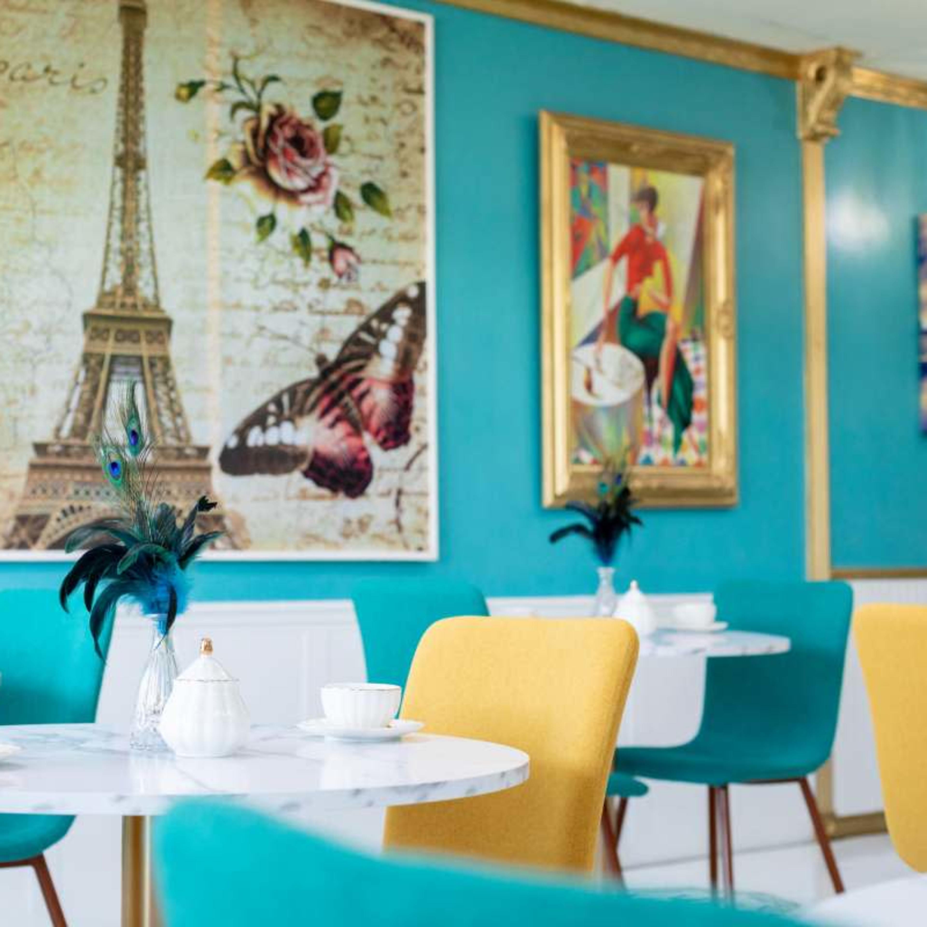 A brightly decorated café with marble tables, colorful chairs, and wall art that includes the Eiffel Tower and floral motifs.