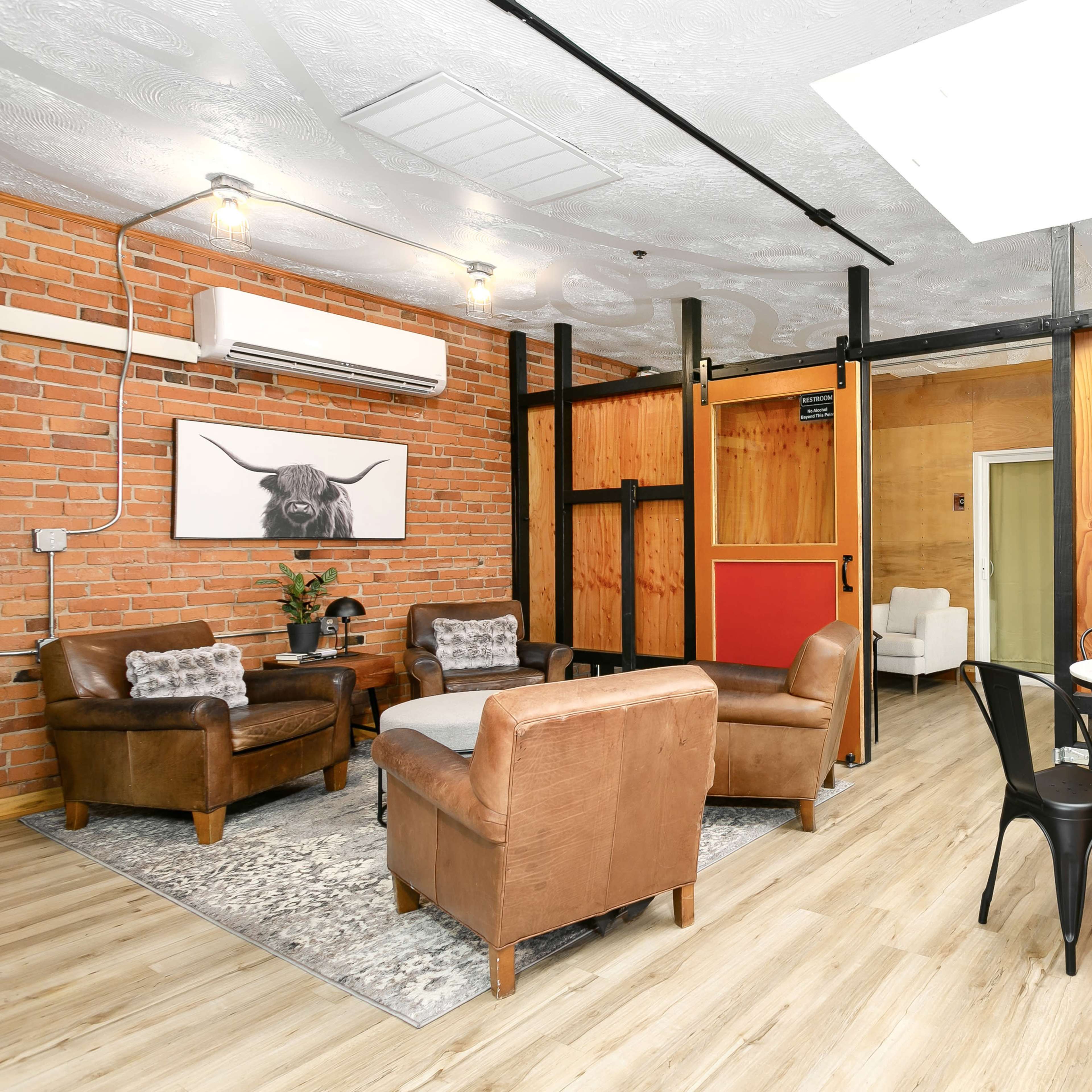 A spacious room featuring brown leather chairs, a round table with black chairs, and a mix of brick and wooden walls.