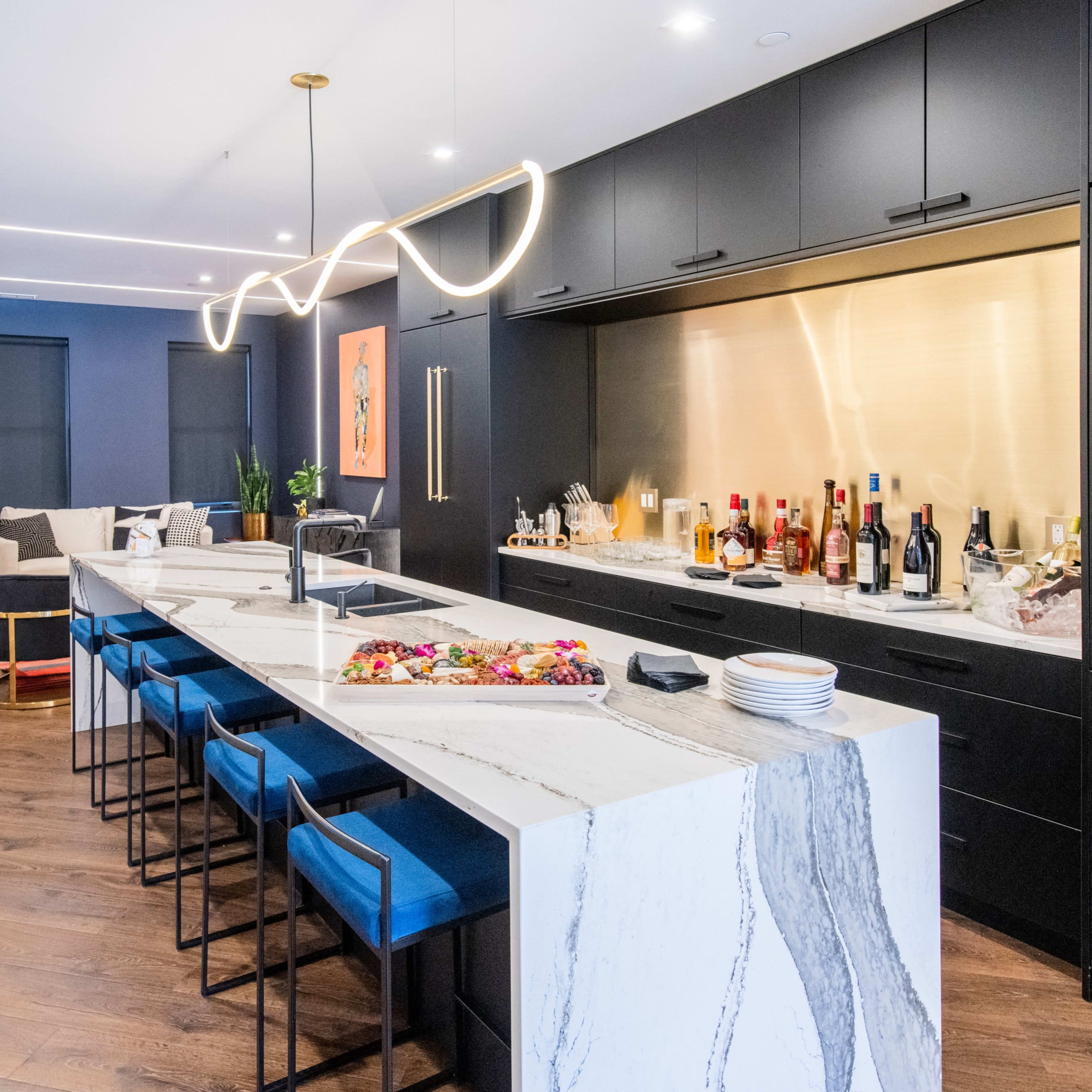 A modern kitchen with a large marble island, black cabinetry, and a well-stocked bar area featuring various bottles of spirits.