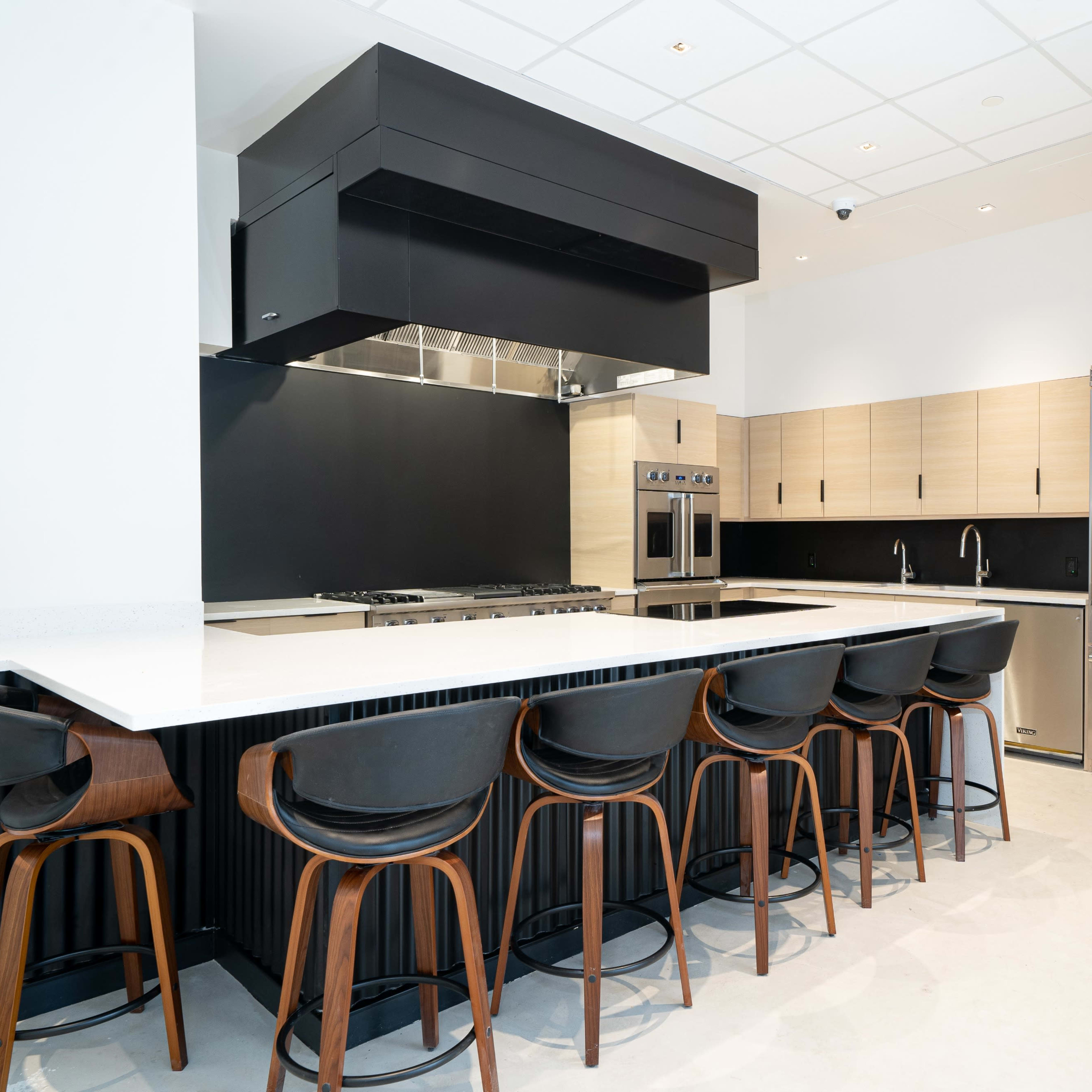 A modern kitchen with a black and wooden color scheme, featuring a large island with seating and stainless steel appliances.